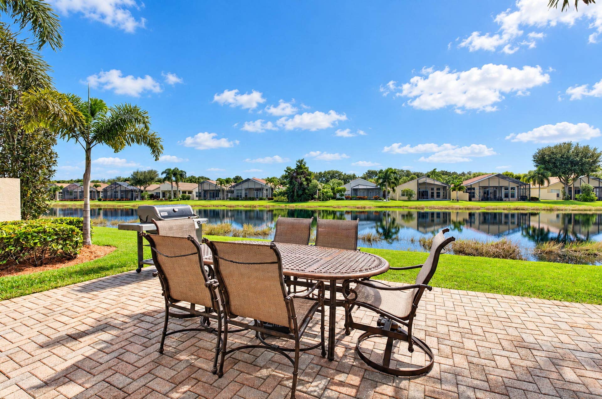 6874 Venidita Beach Drive, Delray Beach, FL 33446 Paver patio featuring a manicured lawn, lake frontage, and mature palm trees