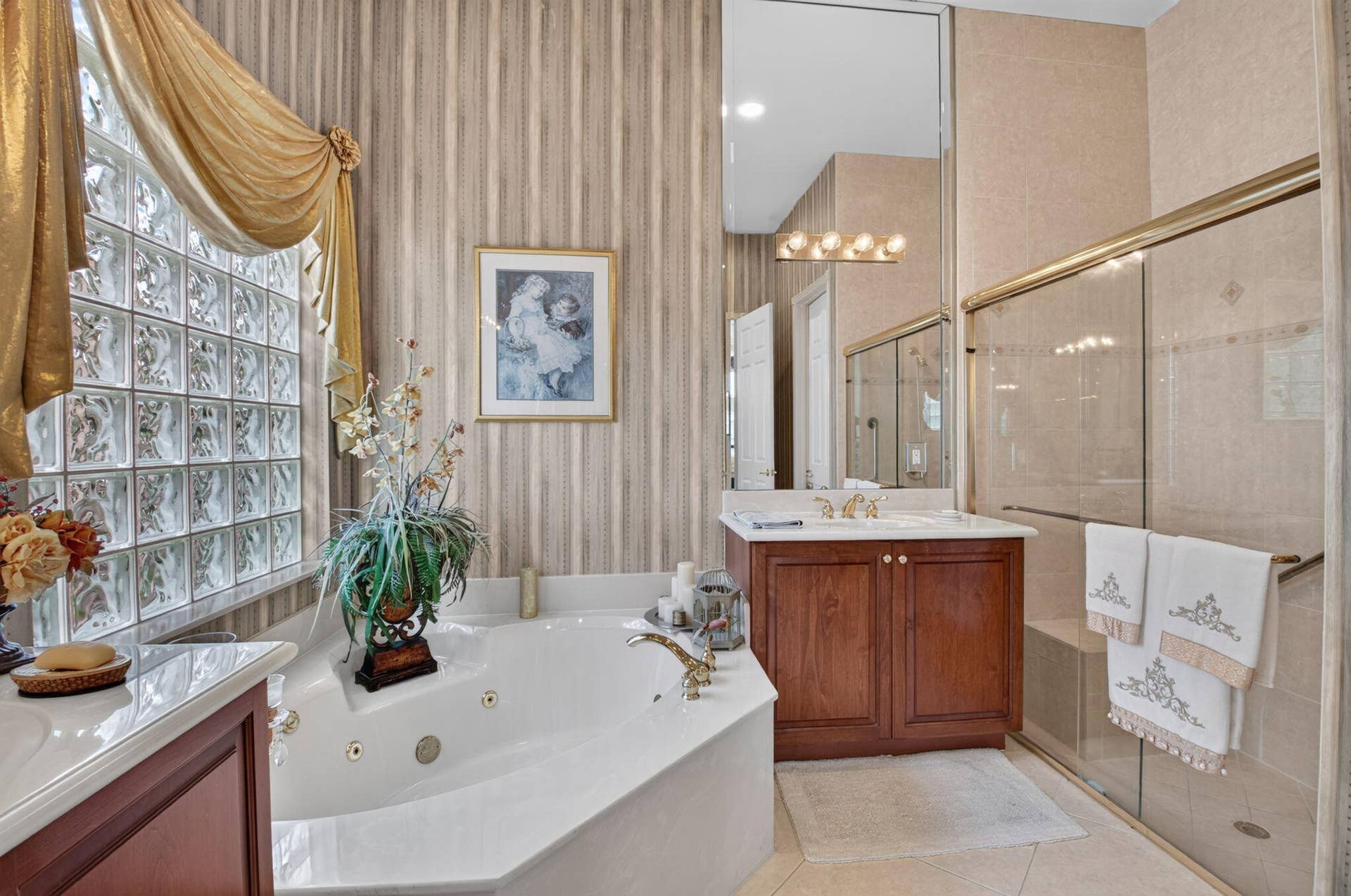 6874 Venidita Beach Drive, Delray Beach, FL 33446 Bathroom featuring a jetted corner soaking tub, glass block window, wood vanity with a stone countertop, and a walk-in shower with a glass enclosure