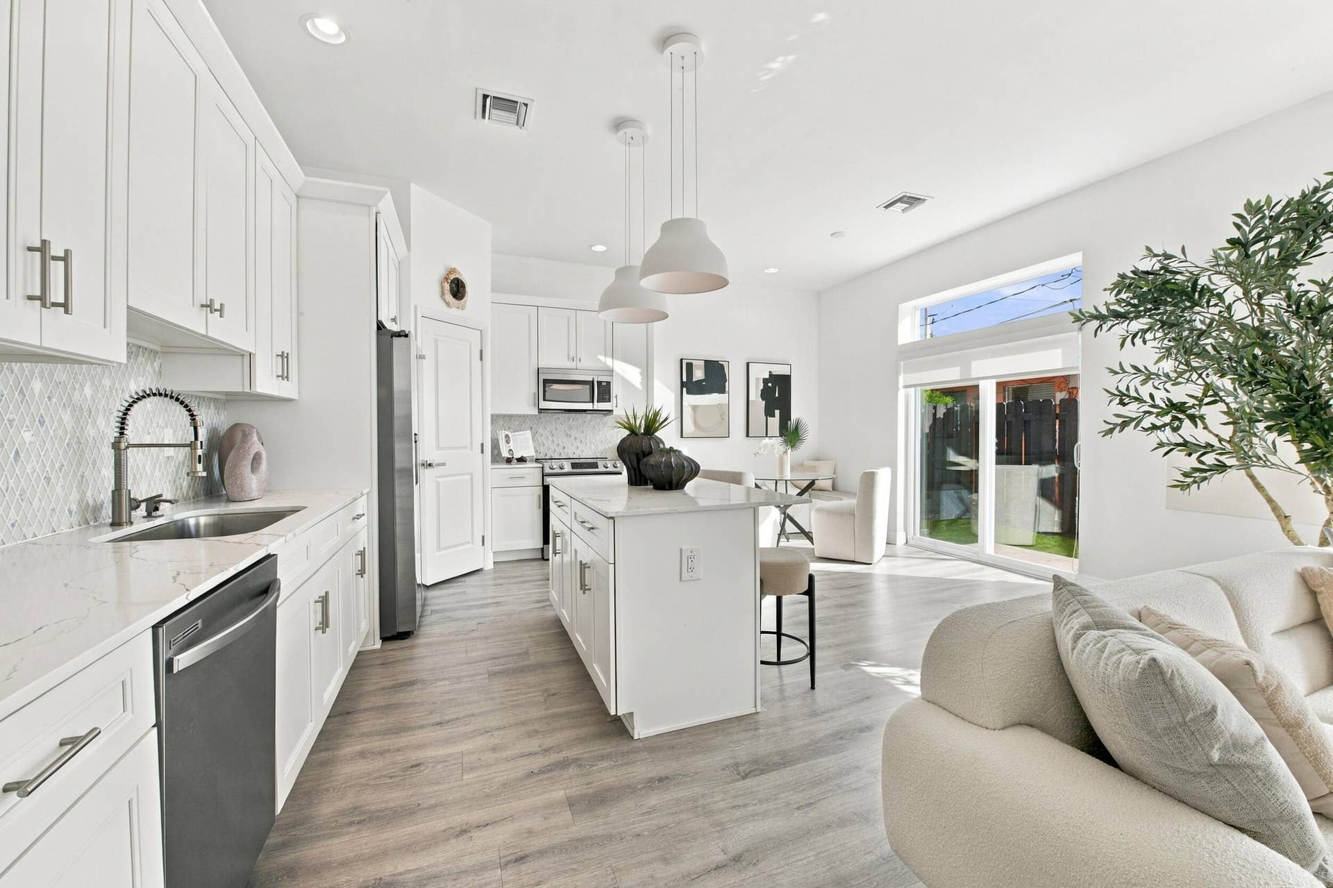 1066 NE 35TH Street, Oakland Park, FL 33334 Kitchen featuring white cabinetry, quartz countertops, a central island with pendant lighting, stainless steel appliances, and wood-finish flooring
