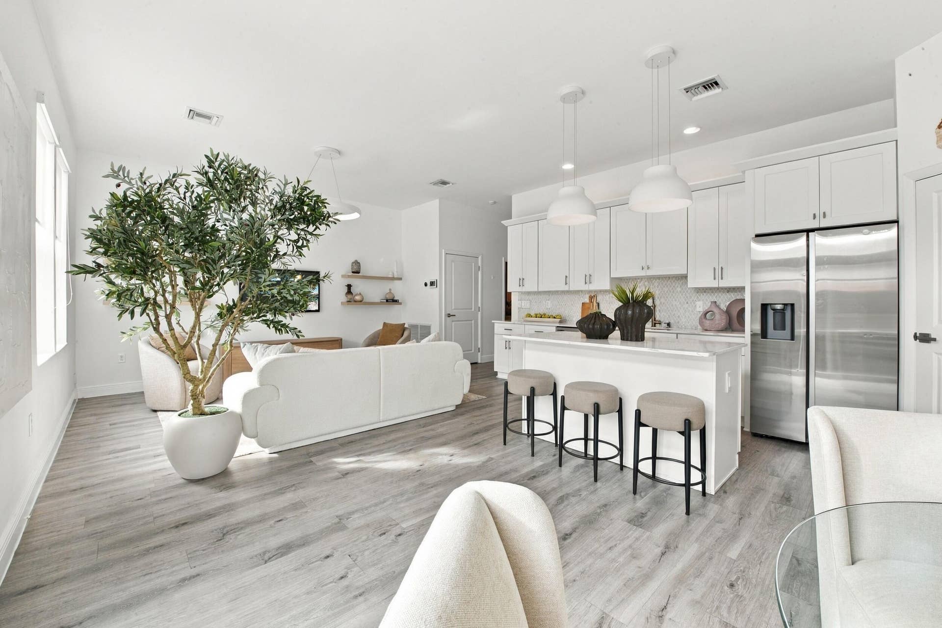 1066 NE 35TH Street, Oakland Park, FL 33334 Open-concept interior featuring wood-finish flooring, white shaker cabinetry, stainless steel refrigerator, kitchen island with seating, and pendant lighting