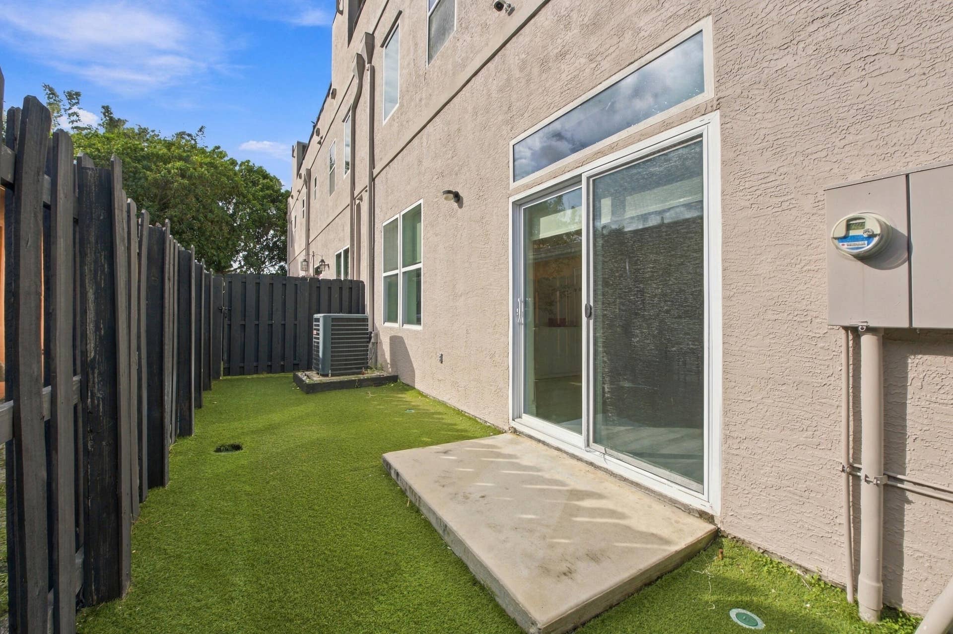 1066 NE 35TH Street, Oakland Park, FL 33334 Private rear courtyard featuring a concrete patio, synthetic turf lawn, and dark-finished vertical privacy fencing