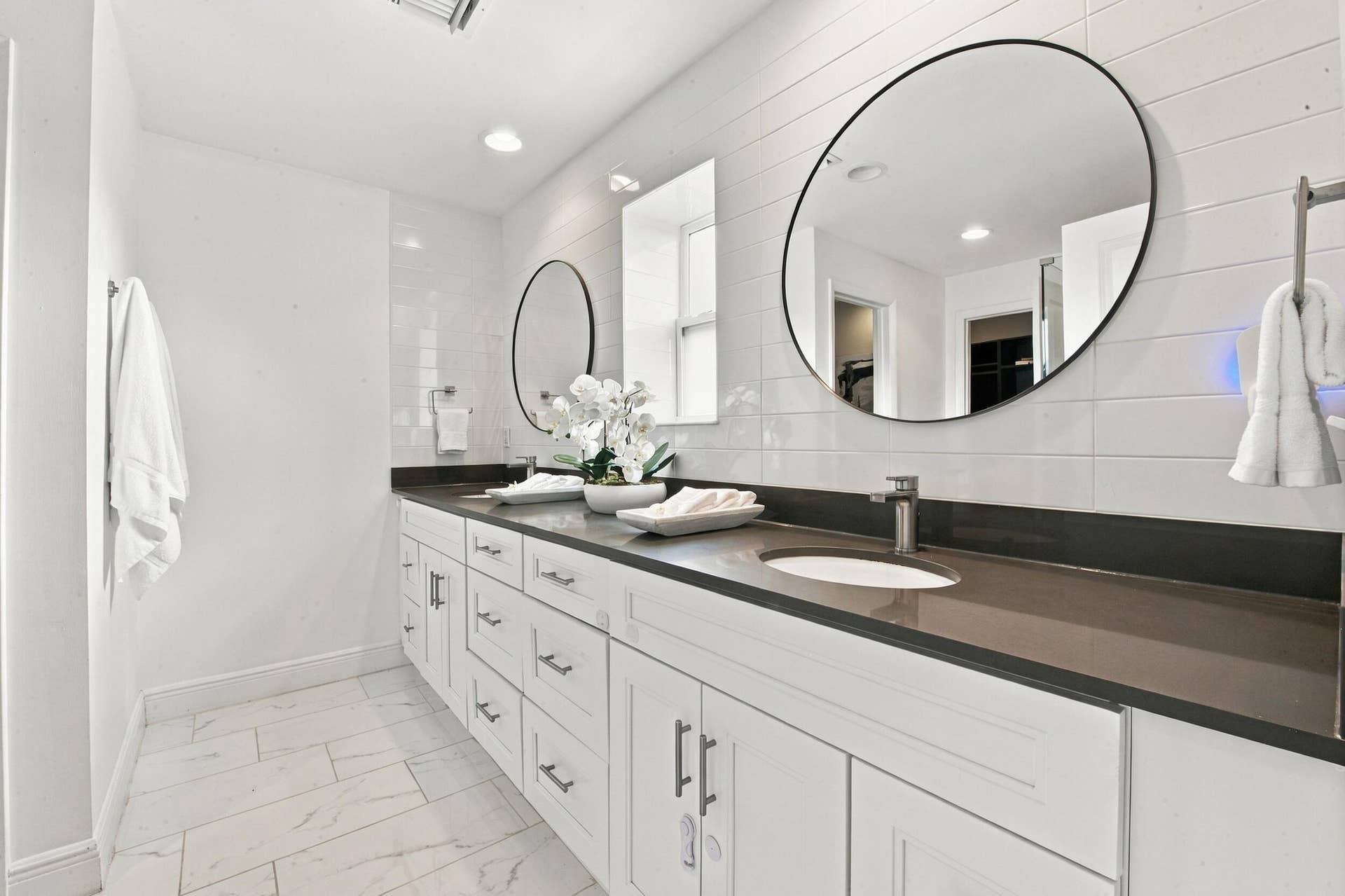 1066 NE 35TH Street, Oakland Park, FL 33334 Dual-sink vanity featuring white cabinetry, a solid-surface countertop, rectangular undermount sinks, wall-mounted round mirrors, and tile flooring