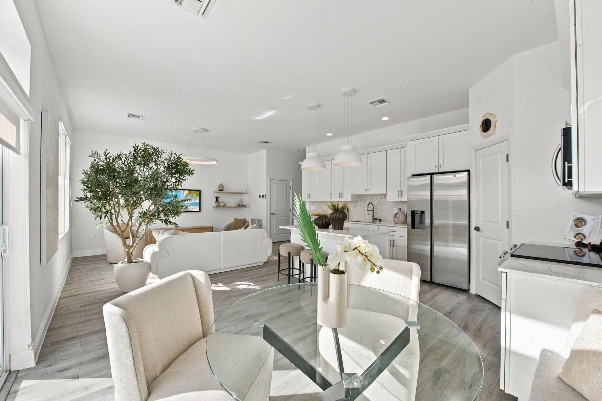 1066 NE 35TH Street, Oakland Park, FL 33334 Open-concept kitchen featuring white shaker-style cabinetry, quartz countertops, a waterfall-edge center island, stainless steel appliances, and wood-finish flooring