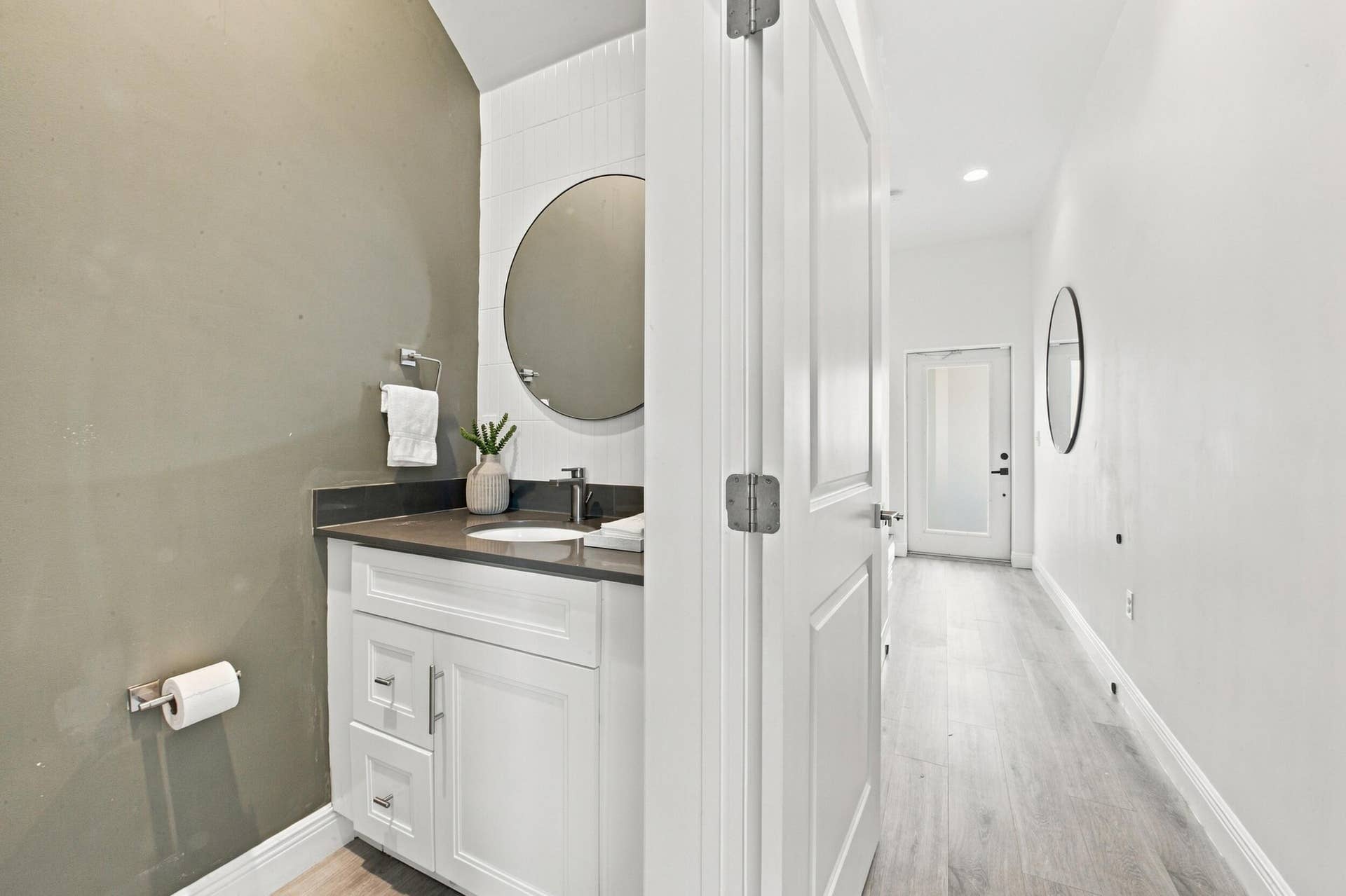 1066 NE 35TH Street, Oakland Park, FL 33334 Powder room featuring a white vanity cabinet, solid surface countertop with an integrated basin, round wall-mounted mirror, and wood-finish flooring