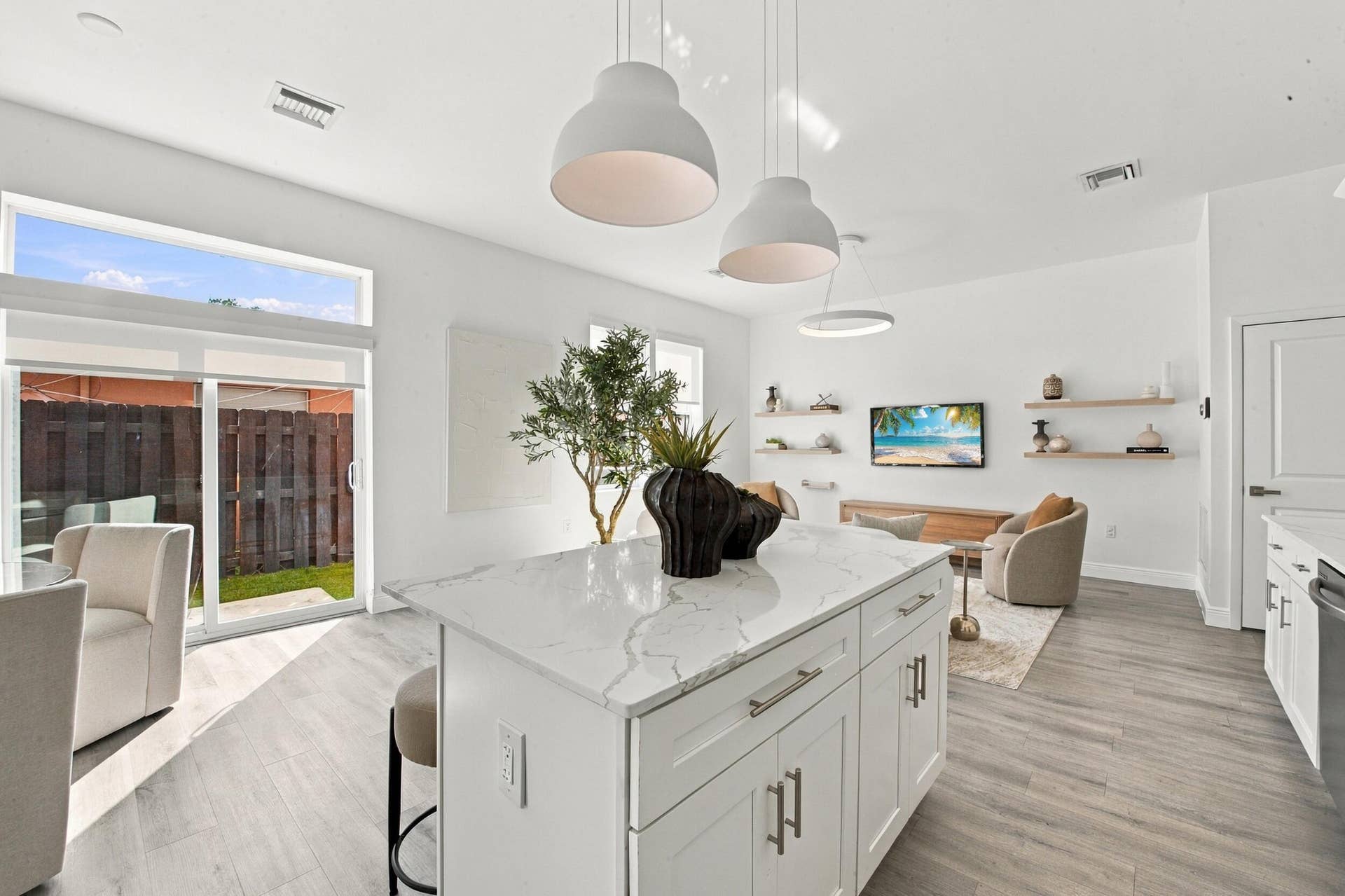 1066 NE 35TH Street, Oakland Park, FL 33334 Kitchen featuring a central island with stone-patterned countertop, wood-finish flooring, white cabinetry, overhead pendant lighting, and sliding glass doors