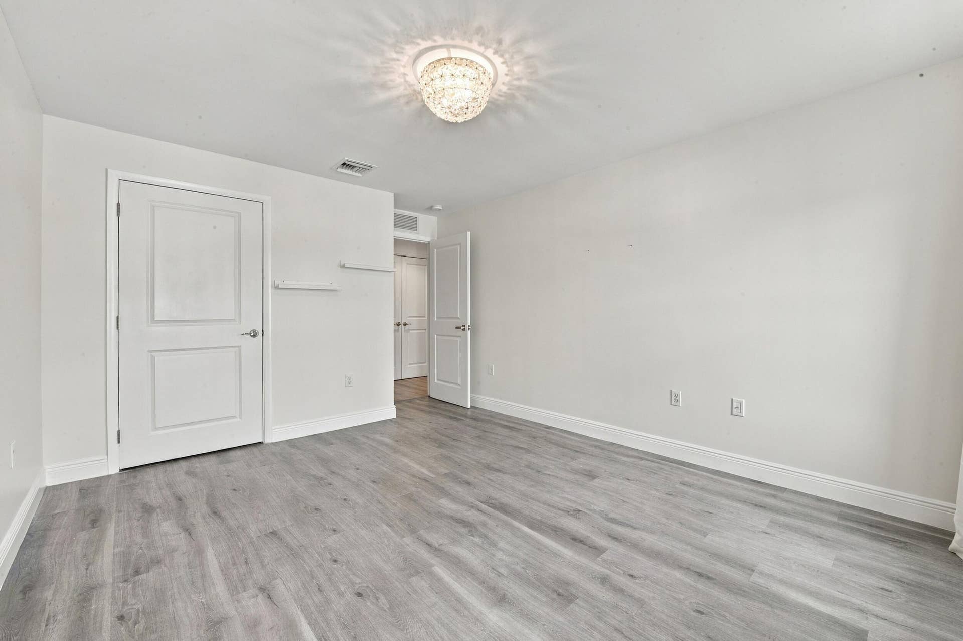 1066 NE 35TH Street, Oakland Park, FL 33334 Room interior featuring wood-finish flooring, a multi-tiered crystal flush-mount light fixture, and two panel doors