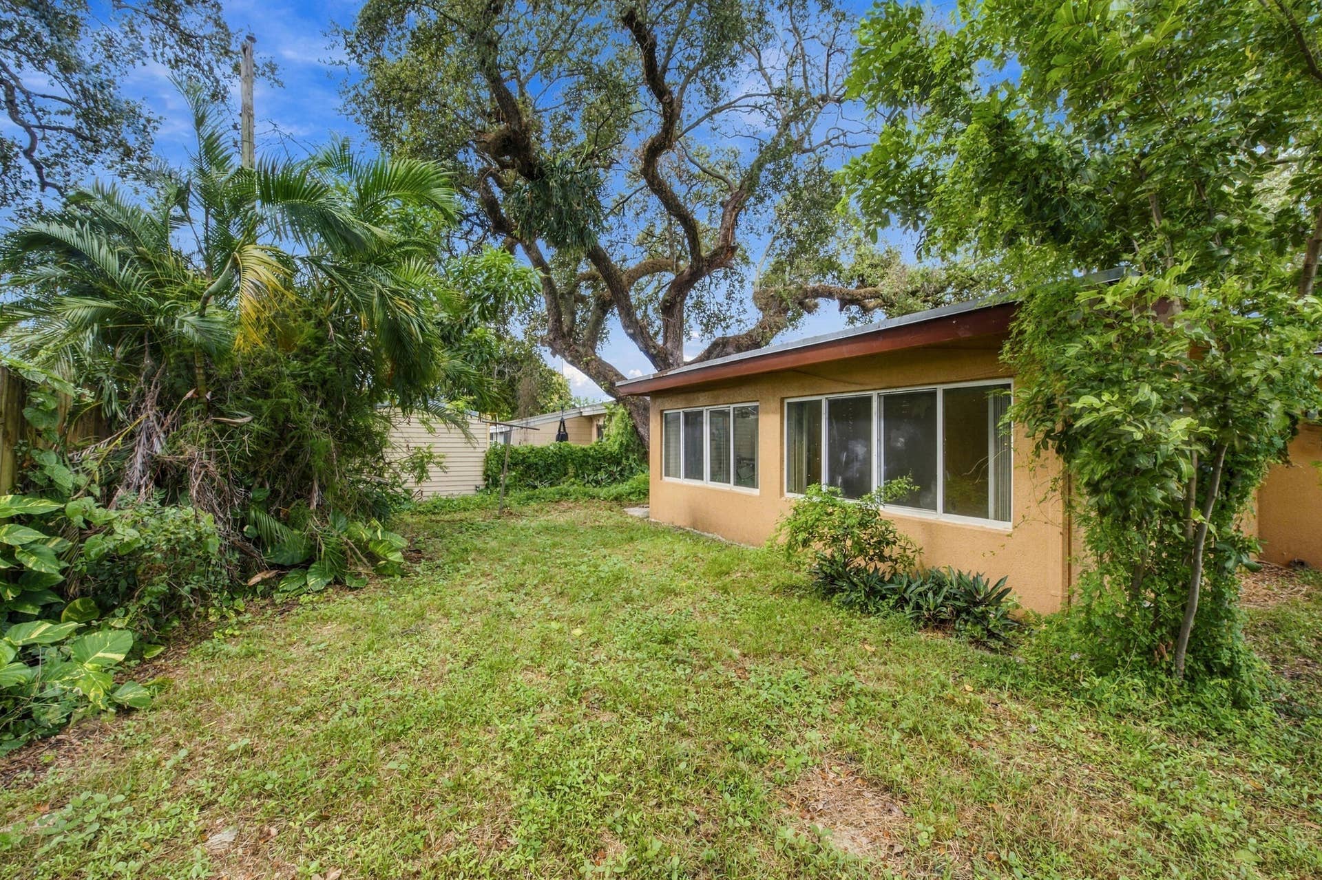 6660 FREEDOM Street, Hollywood, FL 33024 Exterior featuring a stucco-finish facade, large windows with white frames, mature trees, and landscaping
