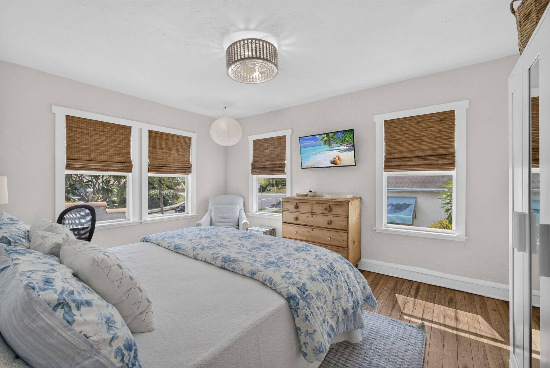 Room featuring wood-finish flooring, multiple windows with white trim, and a decorative drum-style ceiling light fixture