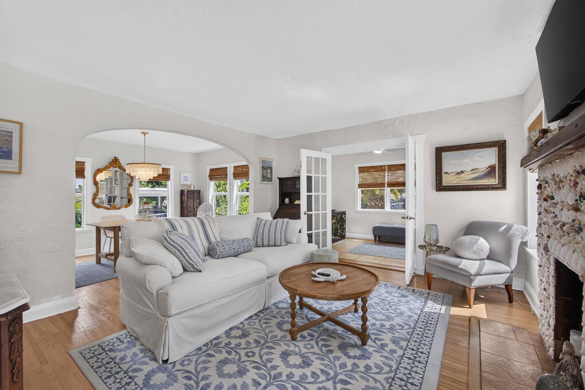 Living space featuring wood-finish flooring, a textured stone fireplace surround, an arched architectural opening, and multi-pane French doors