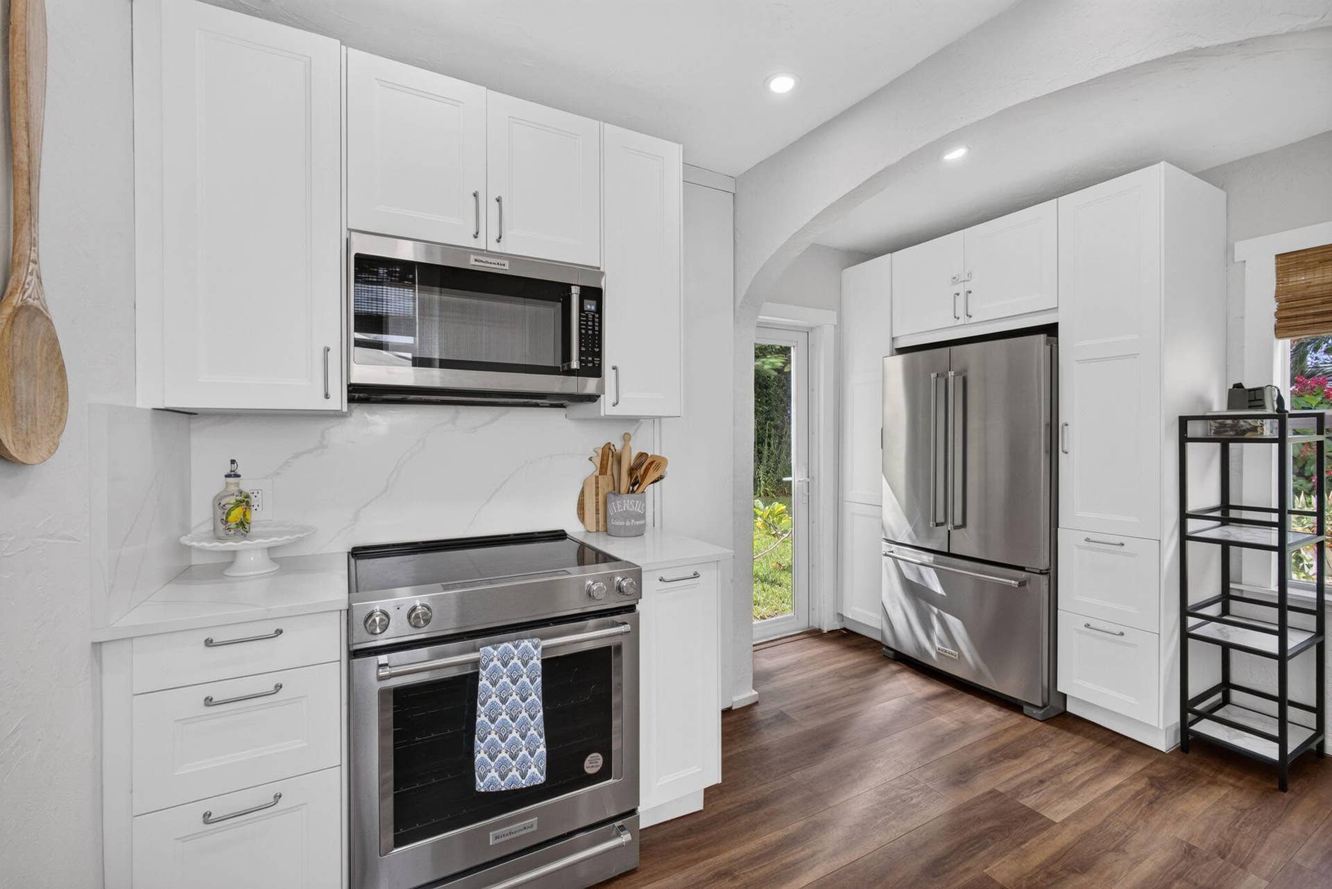 Kitchen featuring white shaker-style cabinetry, stainless steel appliances, solid-surface countertops, stone-patterned backsplash, and wood-finish flooring
