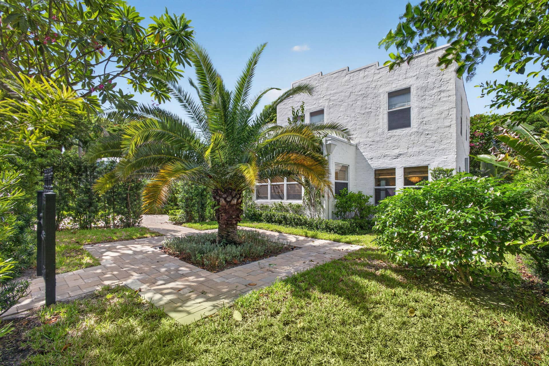 Two-story exterior featuring white textured masonry, multi-pane windows, a paver walkway, and mature landscaping