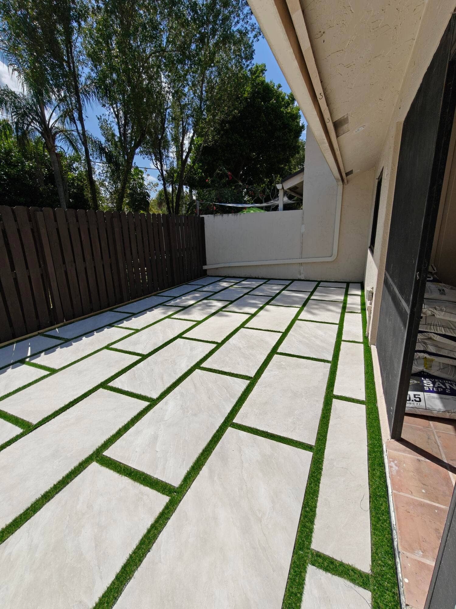 2700 S OAKLAND FOREST Drive, #603, Oakland Park, FL 33309 Paver patio featuring large-format concrete tiles with synthetic turf ribbon accents and a privacy wood fence