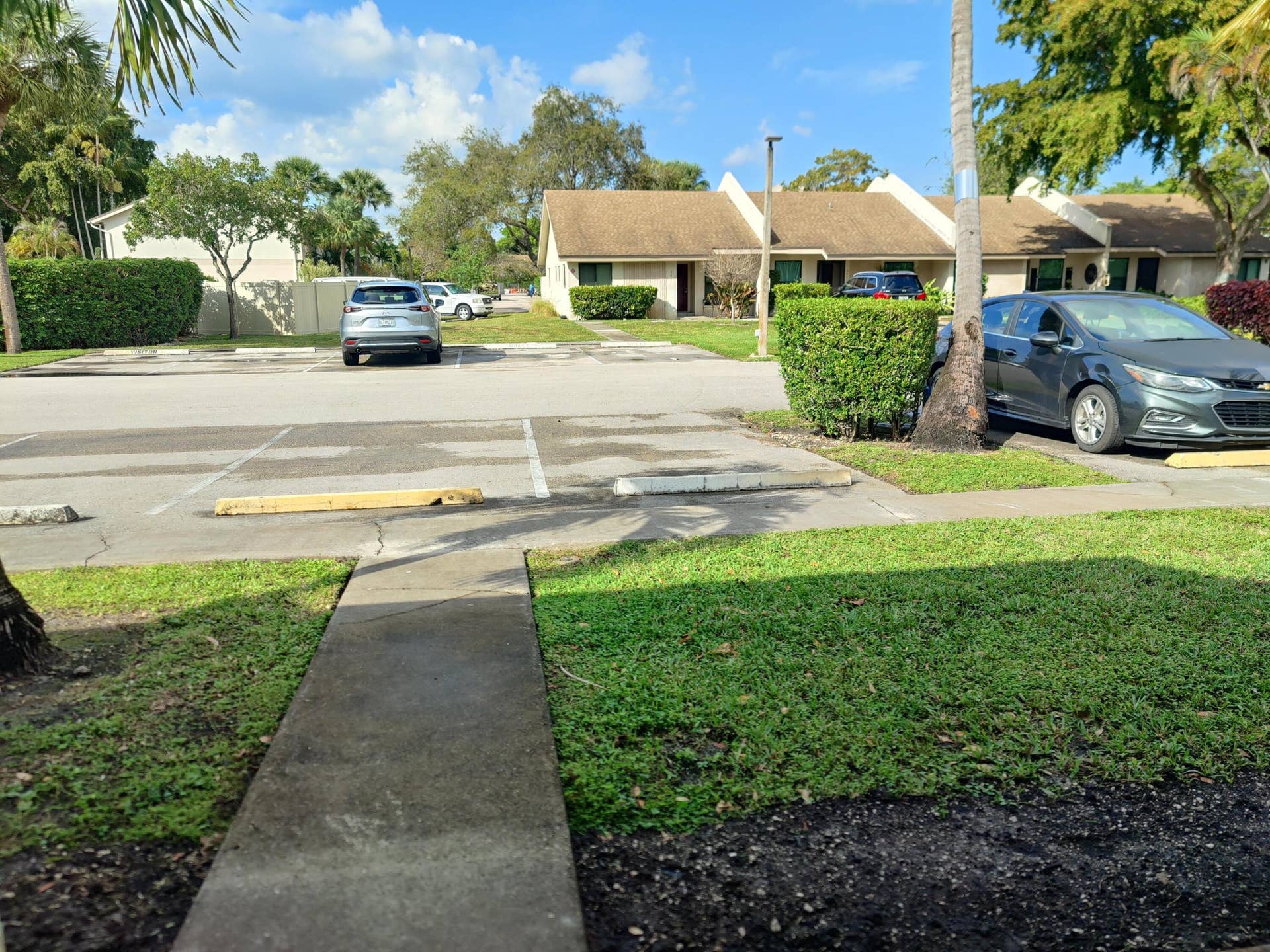 2700 S OAKLAND FOREST Drive, #603, Oakland Park, FL 33309 Asphalt parking area featuring designated spaces with concrete wheel stops, manicured lawn, and concrete walkways