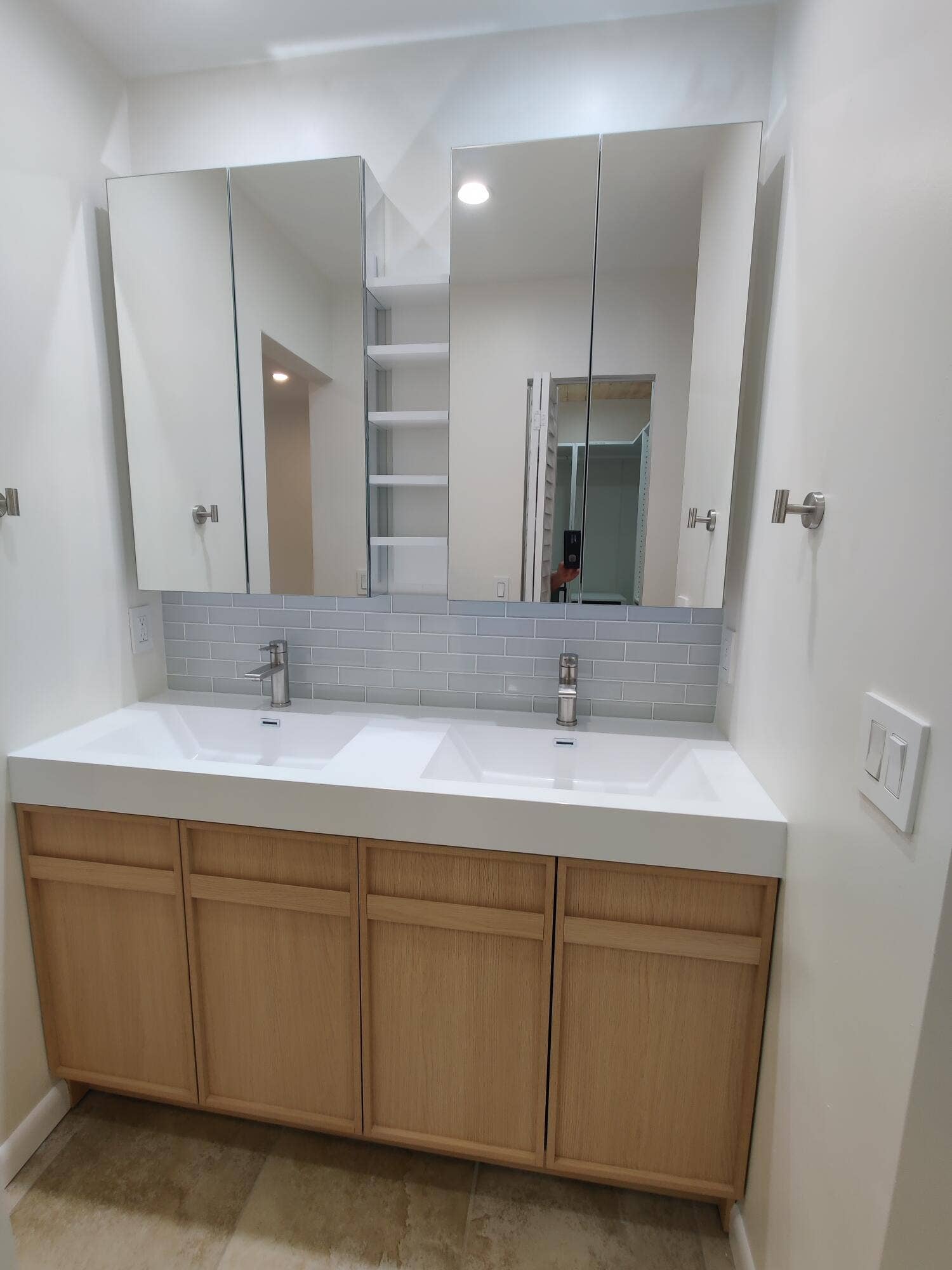 2700 S OAKLAND FOREST Drive, #603, Oakland Park, FL 33309 Double vanity featuring a white integrated countertop, light wood-finish cabinetry, a glass-tiled backsplash, dual chrome faucets, and mirrored medicine cabinets with integrated shelving