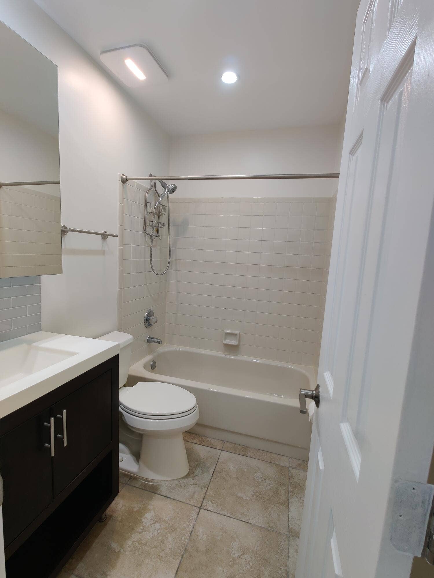 2700 S OAKLAND FOREST Drive, #603, Oakland Park, FL 33309 Bathroom featuring a dark wood-finish vanity with a white countertop, subway tile shower surround, integrated bathtub, and tile flooring