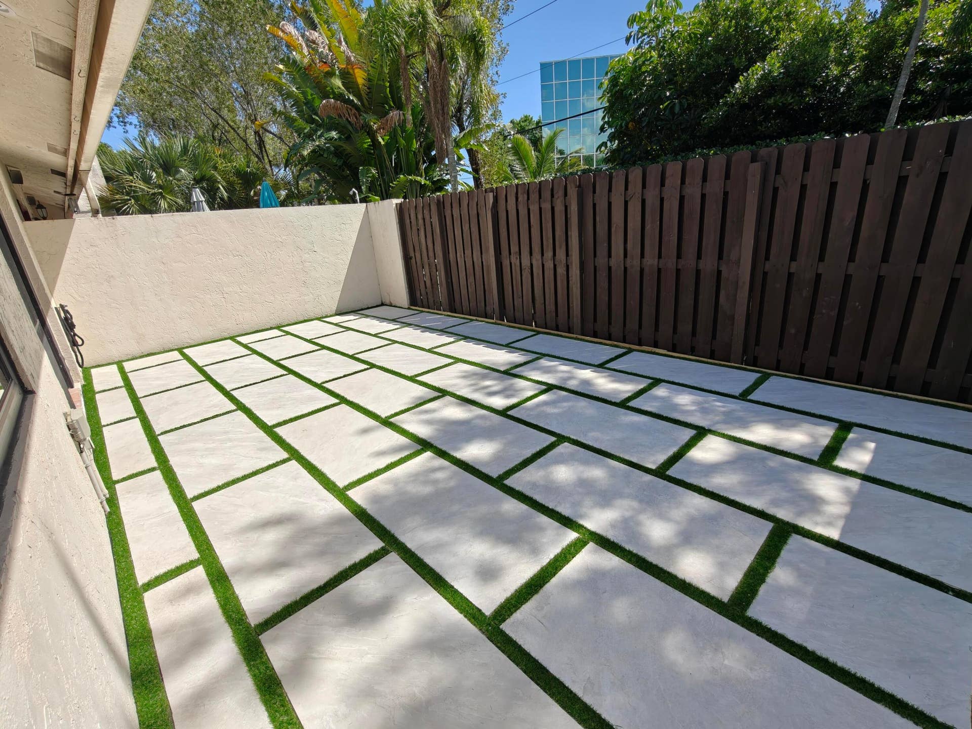 2700 S OAKLAND FOREST Drive, #603, Oakland Park, FL 33309 Private courtyard featuring oversized light-toned concrete pavers, synthetic turf ribbons, and vertical wood privacy fencing