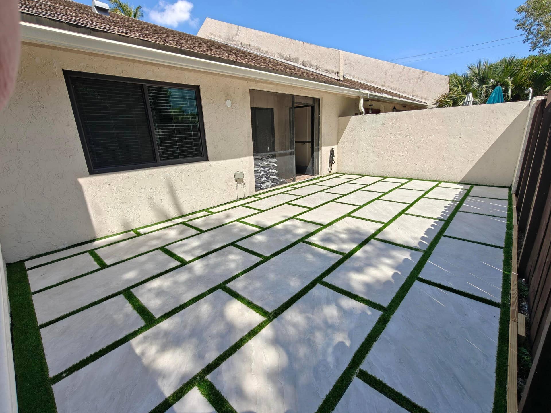 2700 S OAKLAND FOREST Drive, #603, Oakland Park, FL 33309 Private rear courtyard featuring large-format concrete pavers with artificial turf inlay, enclosed by a stucco perimeter wall and a wood-slat fence