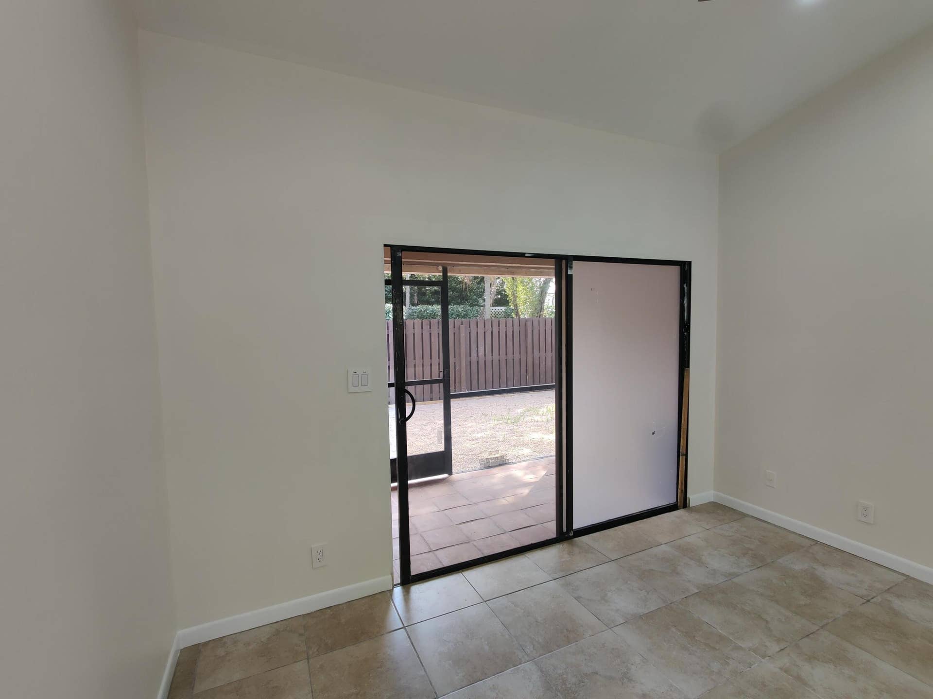 2700 S OAKLAND FOREST Drive, #603, Oakland Park, FL 33309 Vaulted ceiling, ceramic tile flooring, and metal-framed sliding glass doors opening to a tiled patio area with a privacy fence