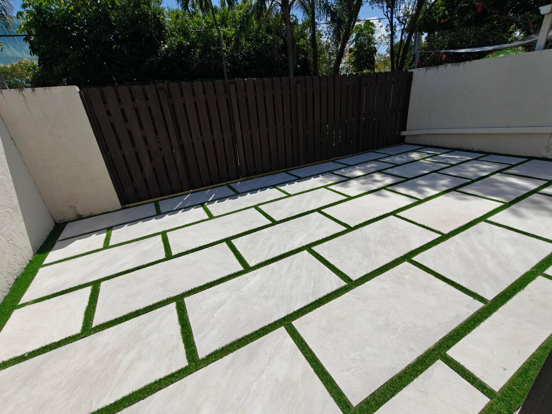 2700 S OAKLAND FOREST Drive, #603, Oakland Park, FL 33309 Outdoor patio featuring oversized light-toned stone pavers, contrasting synthetic turf inlay, and wood-finish privacy fencing