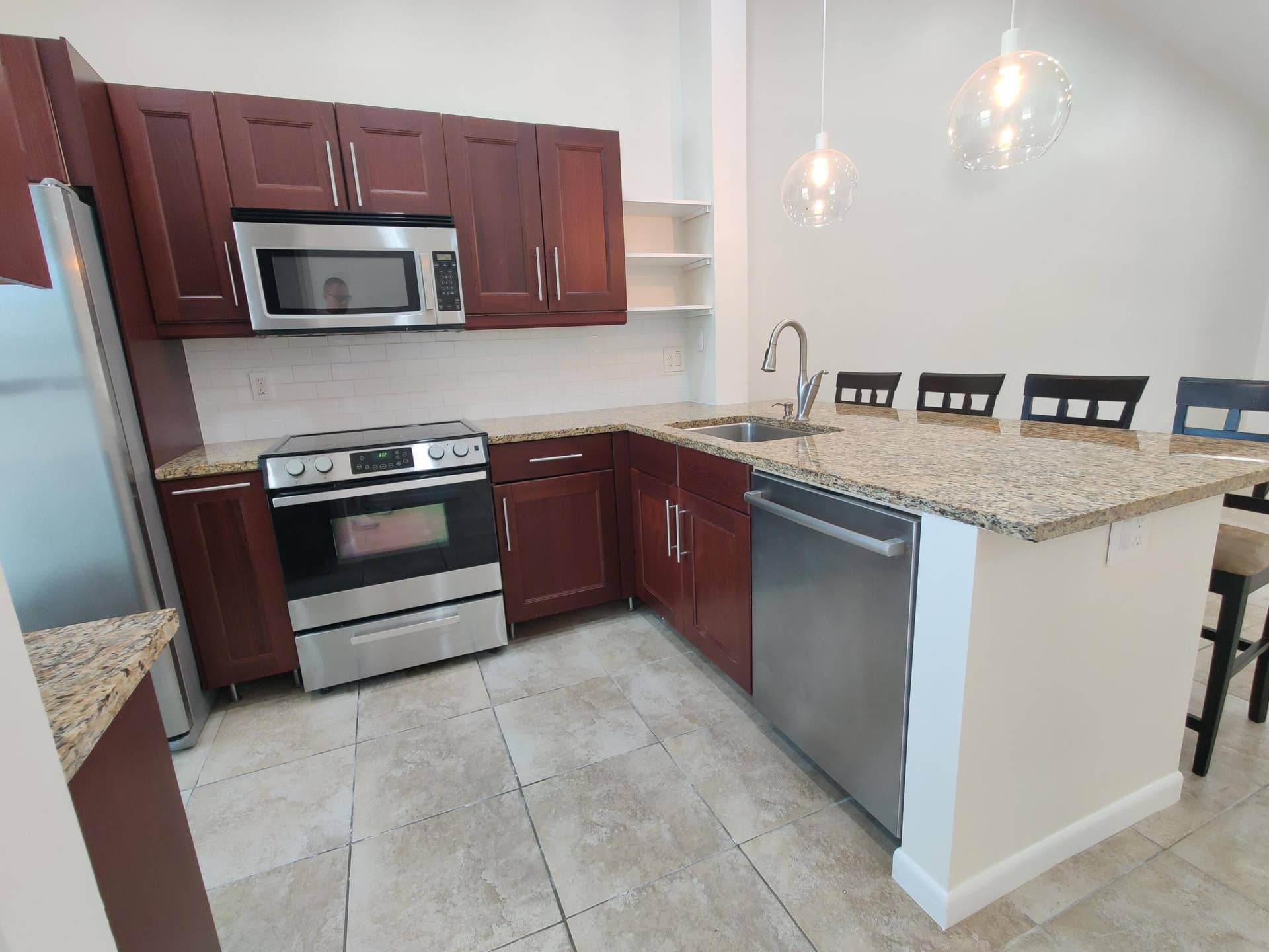 2700 S OAKLAND FOREST Drive, #603, Oakland Park, FL 33309 Kitchen featuring stained wood cabinetry, stone-surface countertops, stainless steel appliances, tile flooring, and pendant lighting
