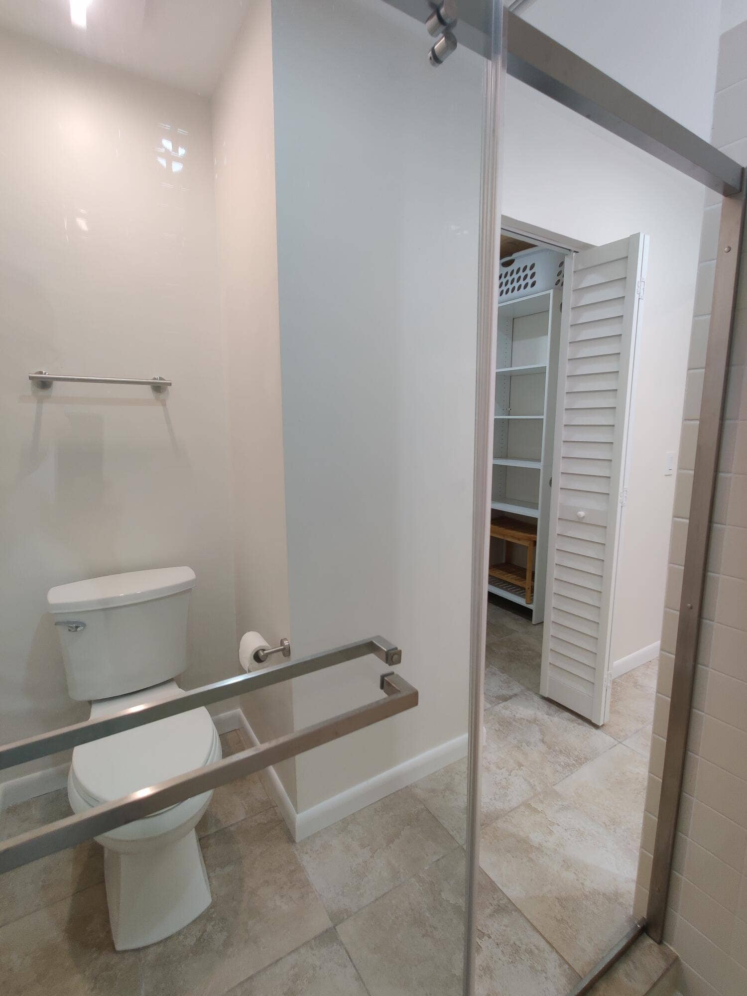 2700 S OAKLAND FOREST Drive, #603, Oakland Park, FL 33309 Bathroom featuring a glass-enclosed shower, light-toned stone-finish tile flooring, a dual-tier metal towel rack, and an entry to a storage space with white louvered doors