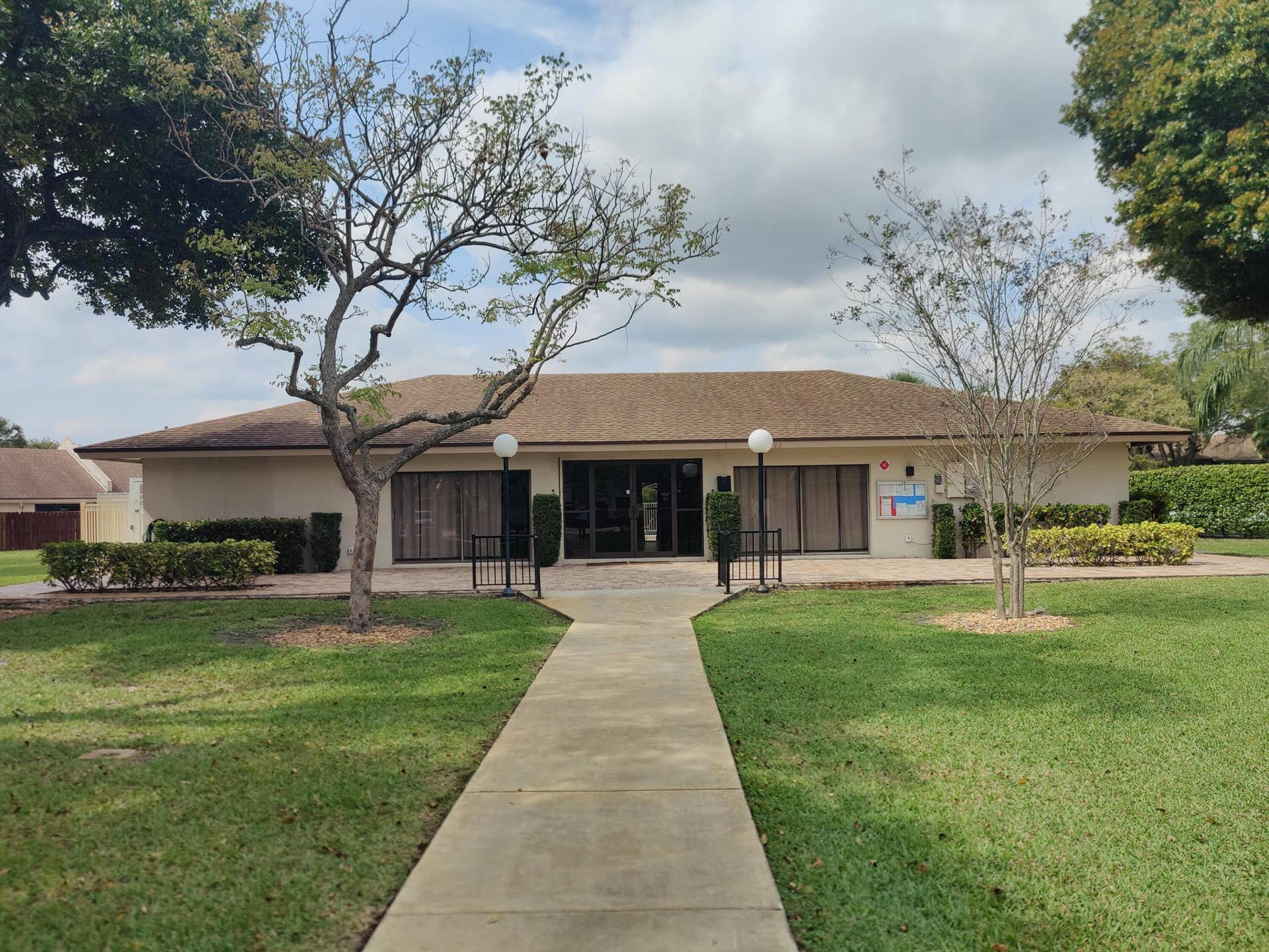 2700 S OAKLAND FOREST Drive, #603, Oakland Park, FL 33309 Single-story exterior featuring a concrete walkway, paved patio, mature trees, manicured landscaping, and globe-style pedestal lighting