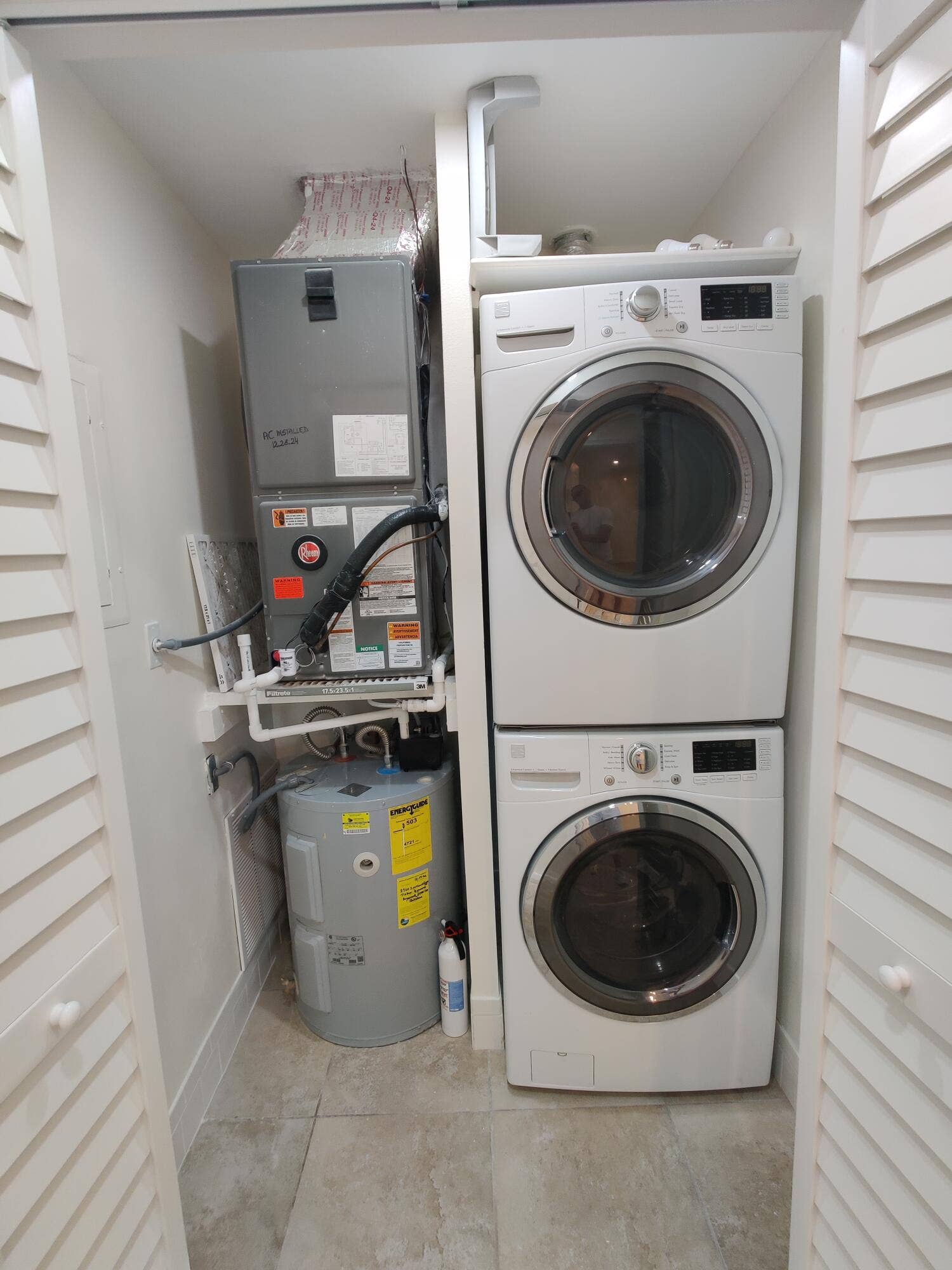 2700 S OAKLAND FOREST Drive, #603, Oakland Park, FL 33309 Utility closet featuring a stacked washer and dryer, an integrated water heater, and a climate control air handler unit, enclosed by louvered bi-fold doors with tiled flooring