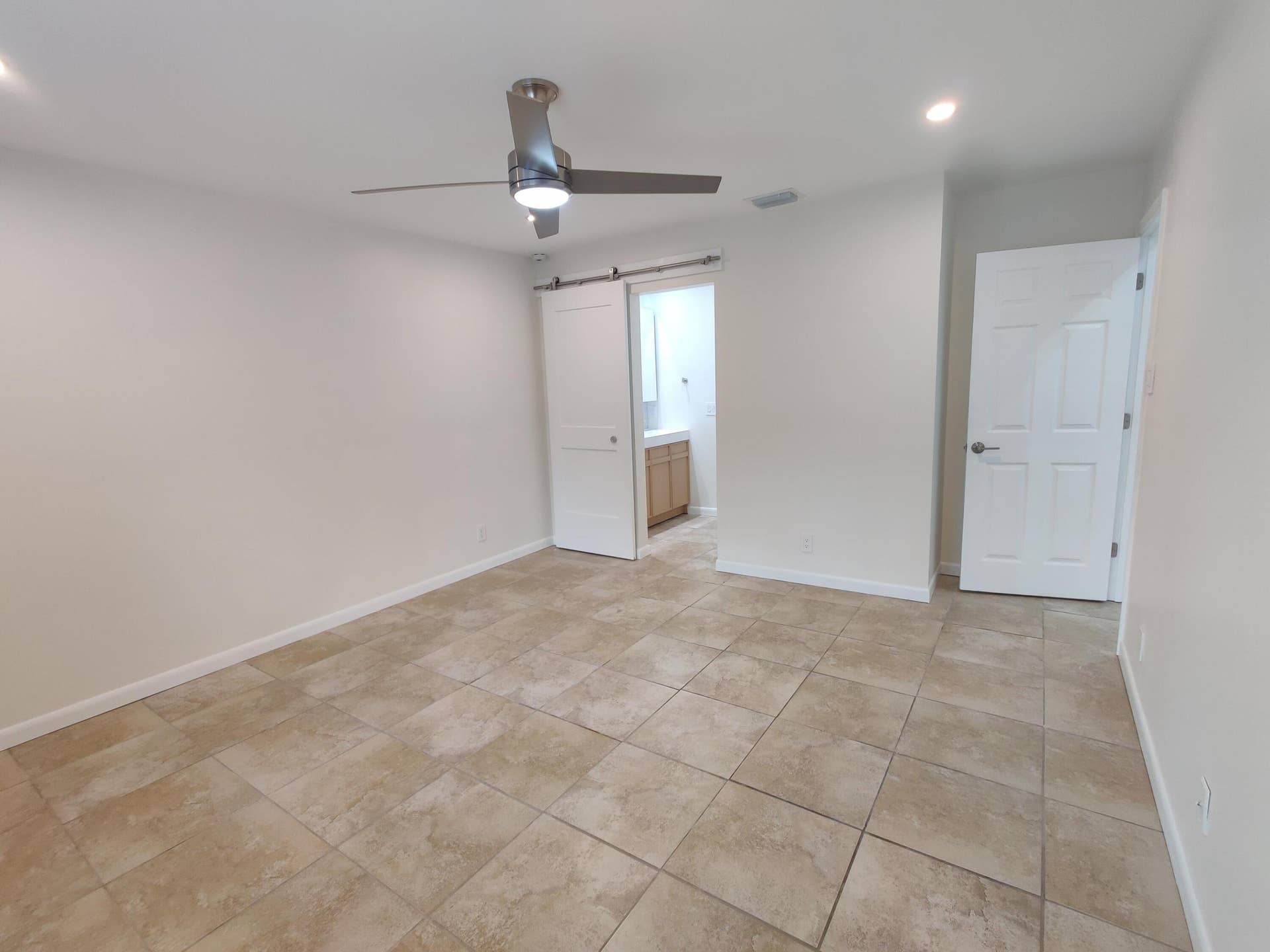 2700 S OAKLAND FOREST Drive, #603, Oakland Park, FL 33309 Neutral-toned tile flooring, brushed metal ceiling fan with integrated lighting, sliding barn-style door, and paneled interior door
