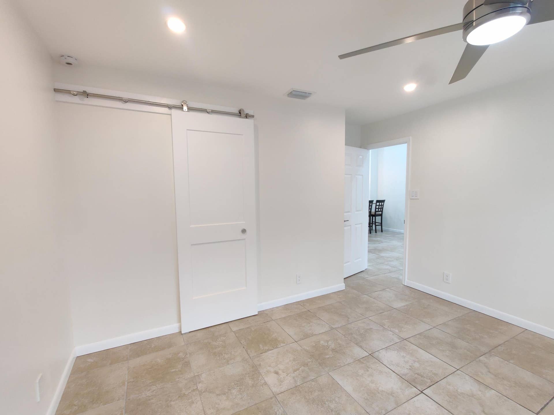 2700 S OAKLAND FOREST Drive, #603, Oakland Park, FL 33309 Interior featuring neutral tile flooring, a white two-panel sliding barn door with stainless steel hardware, and a ceiling fan with integrated lighting