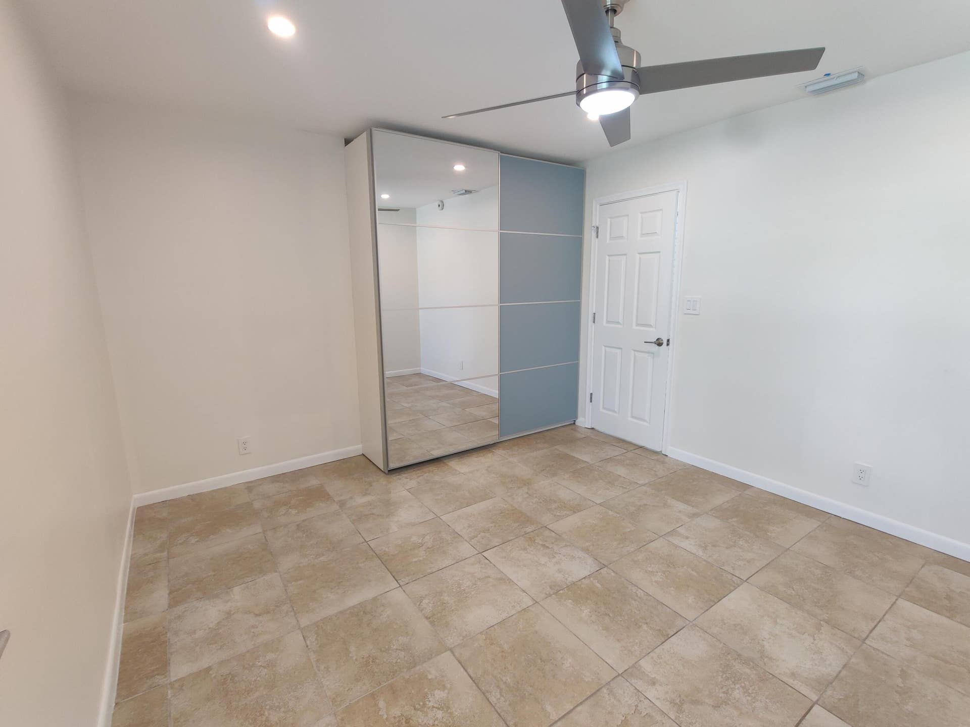 2700 S OAKLAND FOREST Drive, #603, Oakland Park, FL 33309 Large-format tile flooring, built-in floor-to-ceiling wardrobe with mirrored and sliding panels, and a modern brushed-metal ceiling fan with integrated lighting