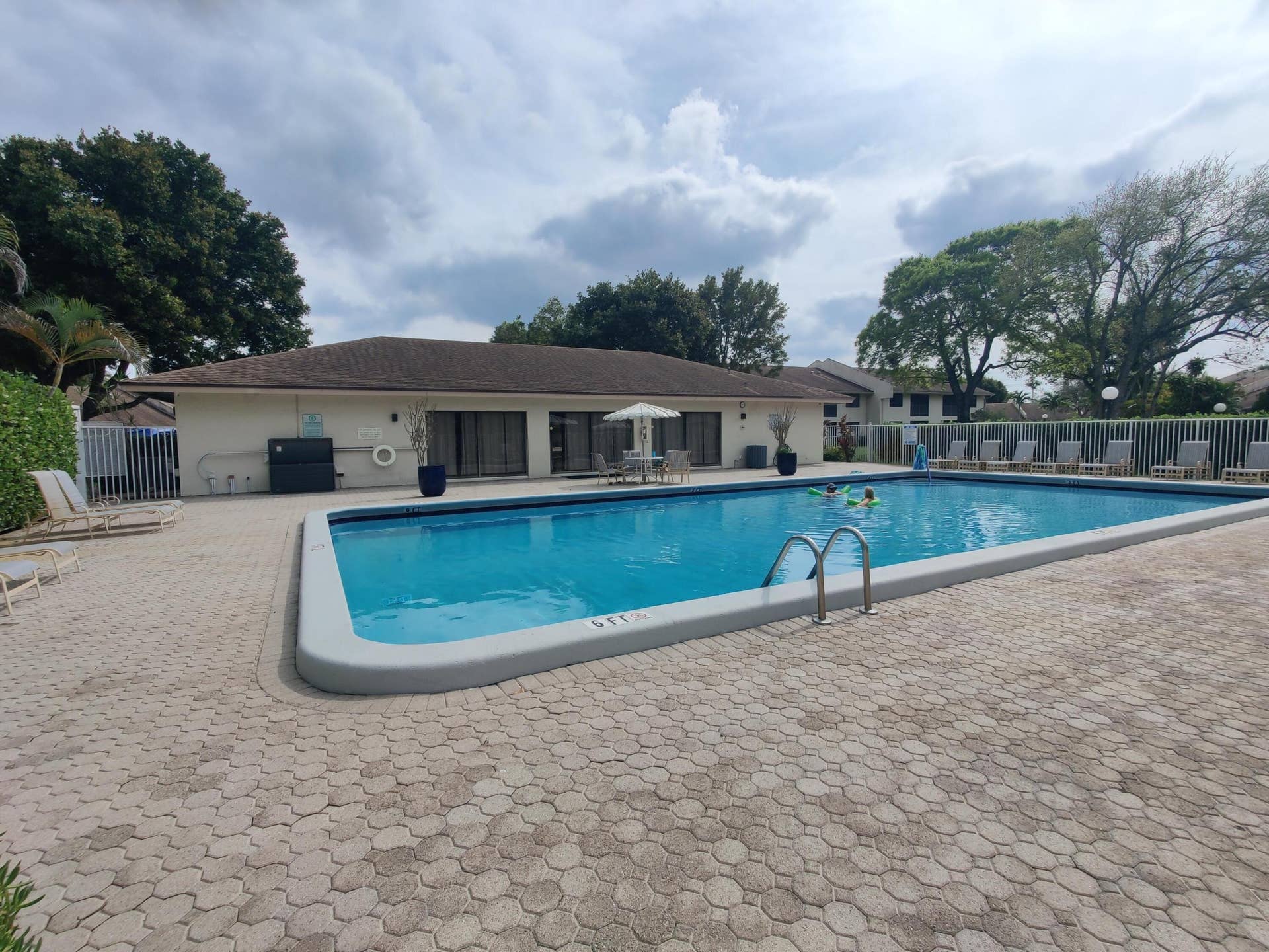 2700 S OAKLAND FOREST Drive, #603, Oakland Park, FL 33309 Rectangular swimming pool featuring a concrete surround, metal entry ladder, expansive paver decking, and perimeter fencing