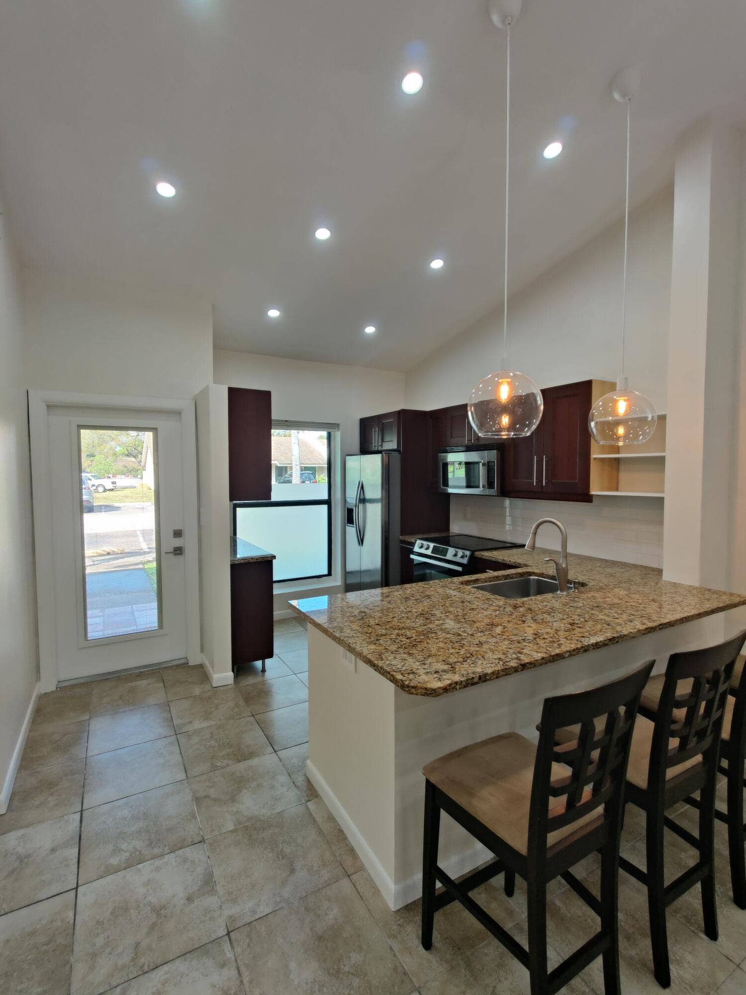 2700 S OAKLAND FOREST Drive, #603, Oakland Park, FL 33309 Kitchen featuring a stone-topped island with an integrated sink, dark wood cabinetry, recessed lighting, glass globe pendant fixtures, and neutral tile flooring