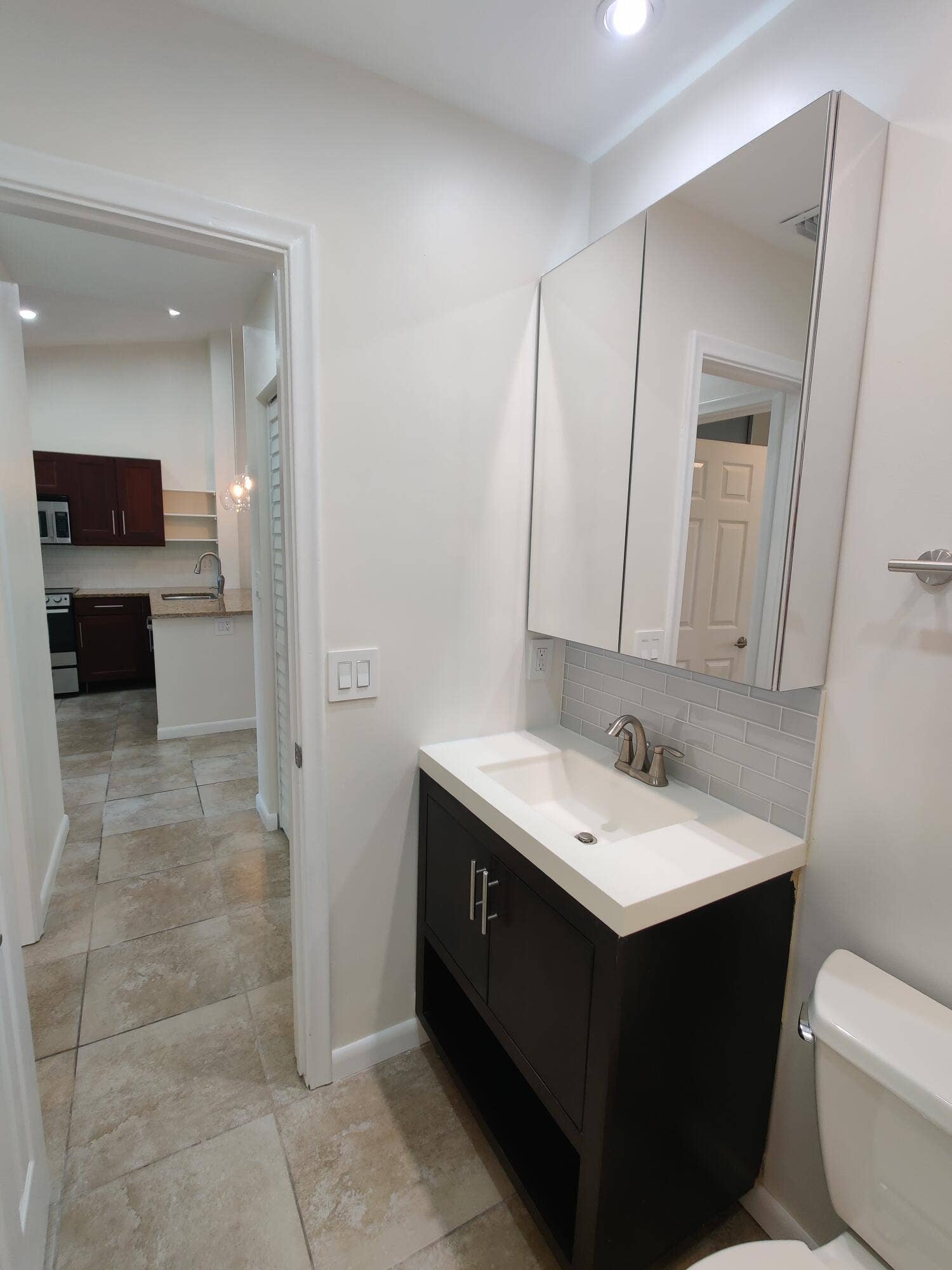 2700 S OAKLAND FOREST Drive, #603, Oakland Park, FL 33309 Dark wood vanity featuring a rectangular integrated sink, neutral stone-finish countertop, mirrored medicine cabinet, and tile backsplash