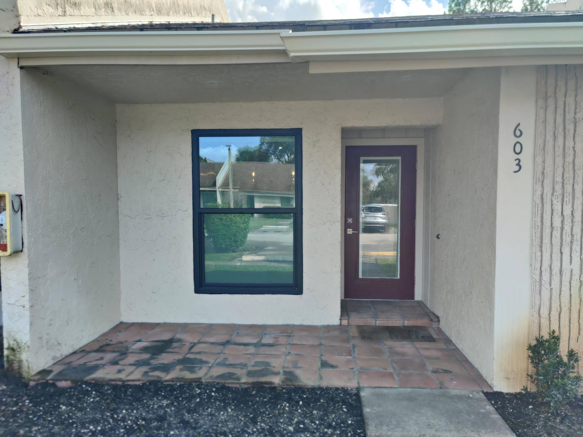 2700 S OAKLAND FOREST Drive, #603, Oakland Park, FL 33309 Covered entrance featuring stucco exterior, terracotta-style tiled porch, single-light glass panel entry door, and dark-framed windows