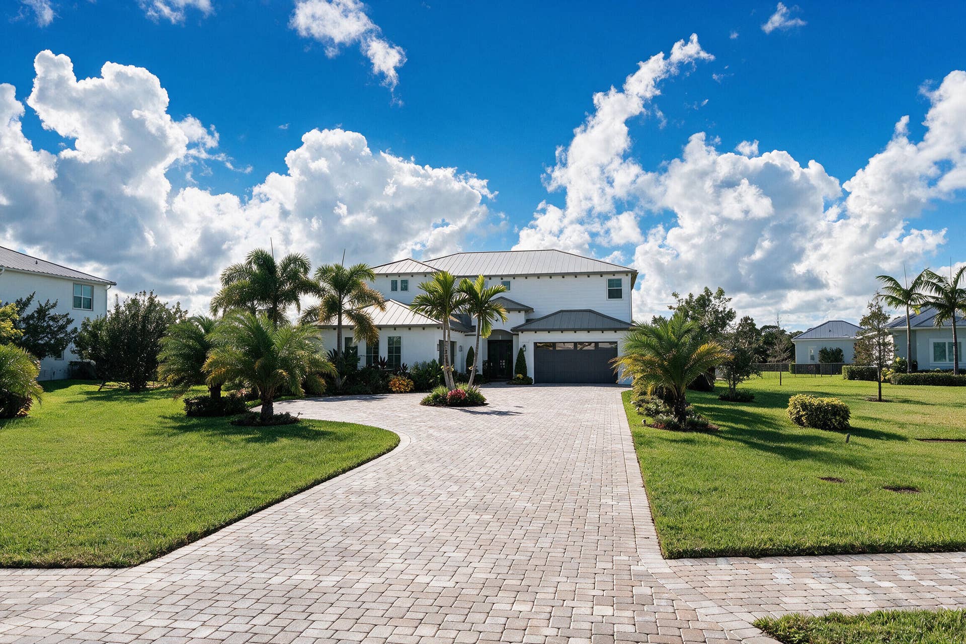 20036 SE BRIDGEWATER Drive, Jupiter, FL 33458 Two-story exterior featuring white stucco siding, a metal roof, an attached garage, and a paver driveway set within a landscaped lawn