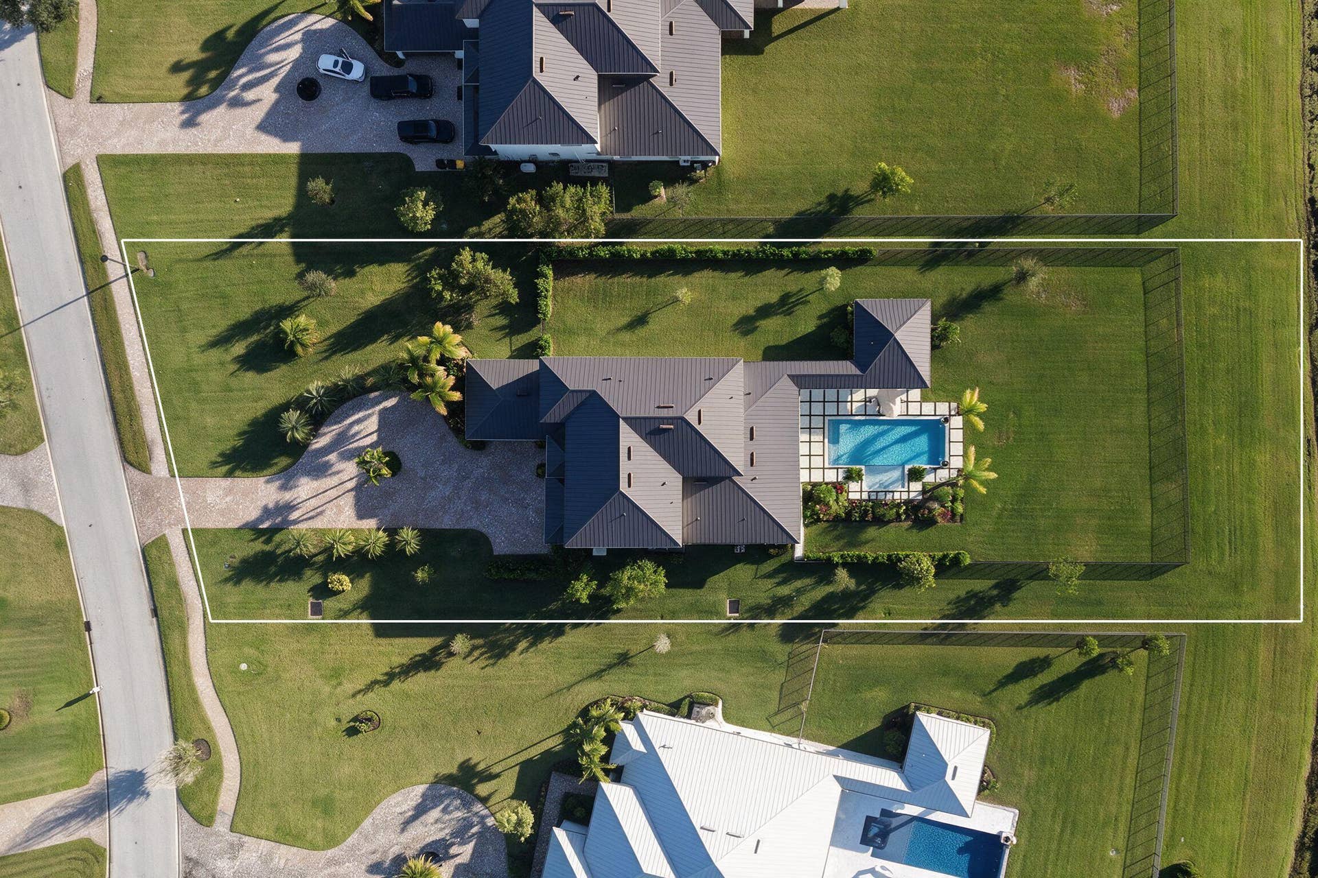 20036 SE BRIDGEWATER Drive, Jupiter, FL 33458 Aerial perspective of a sprawling property featuring a multi-gabled roofline, a paved circular driveway, a rectangular inground pool, and a fully fenced perimeter