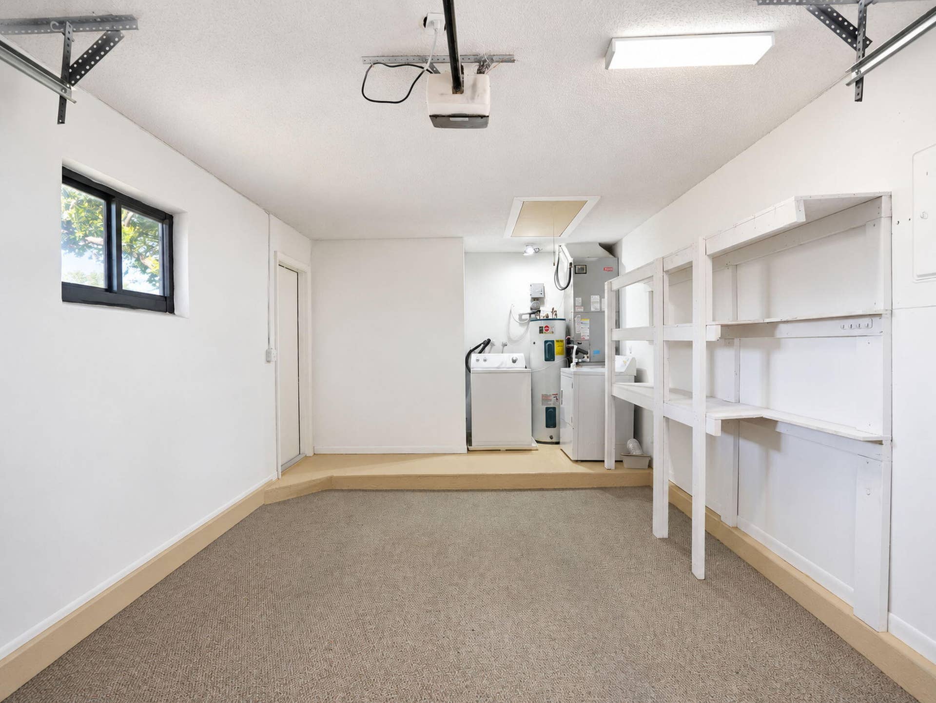 2079 SW 16TH Circle, Deerfield Beach, FL 33442 Enclosed garage space featuring carpeted flooring, a raised utility platform, built-in wall shelving, a single-pane window, and an integrated water heater