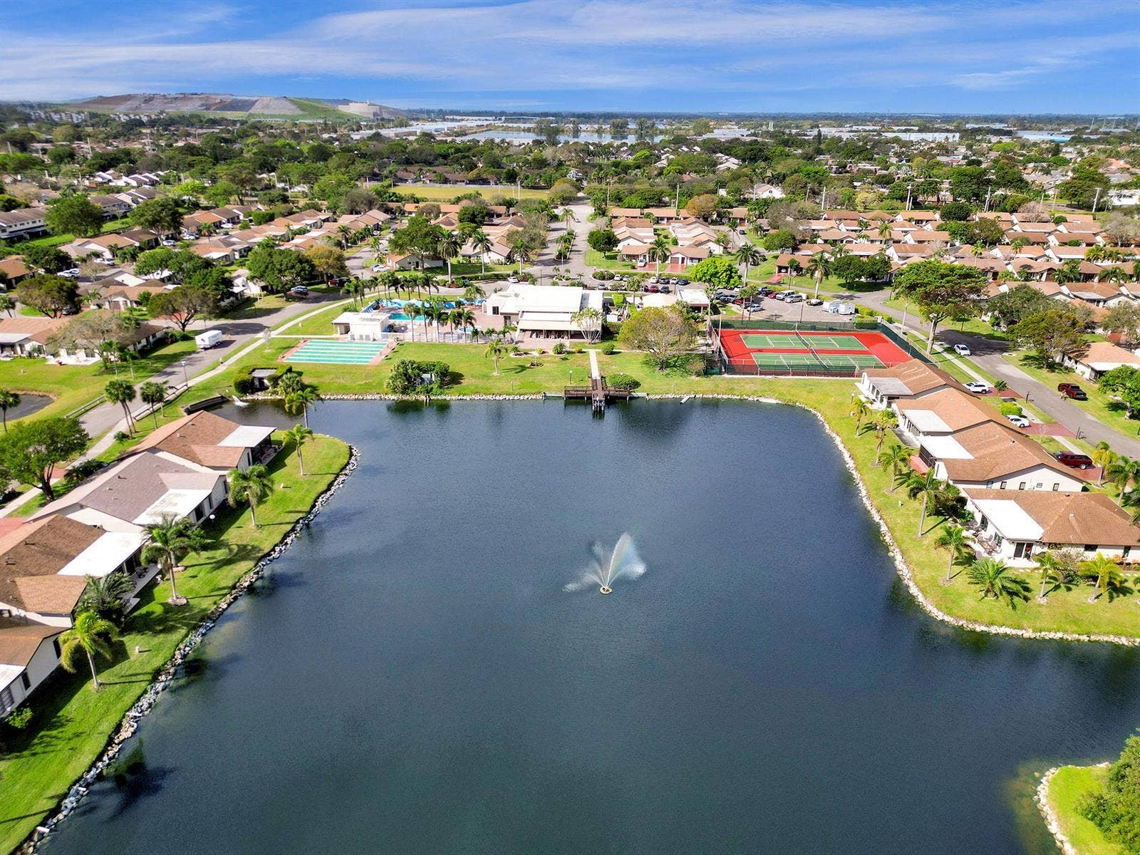 2079 SW 16TH Circle, Deerfield Beach, FL 33442 Aerial perspective of a community featuring a central lake with a fountain, tennis courts, swimming pool, and dedicated clubhouse facilities