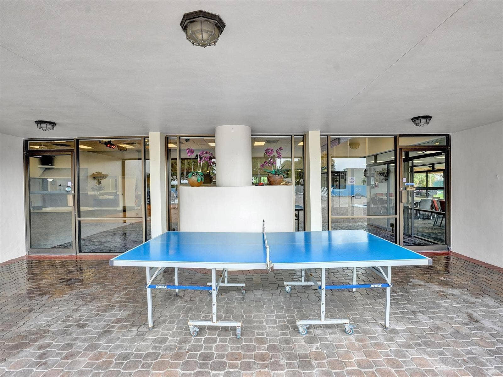 2079 SW 16TH Circle, Deerfield Beach, FL 33442 Covered patio featuring stone-paver flooring, extensive floor-to-ceiling glass paneling, and ceiling-mounted light fixtures