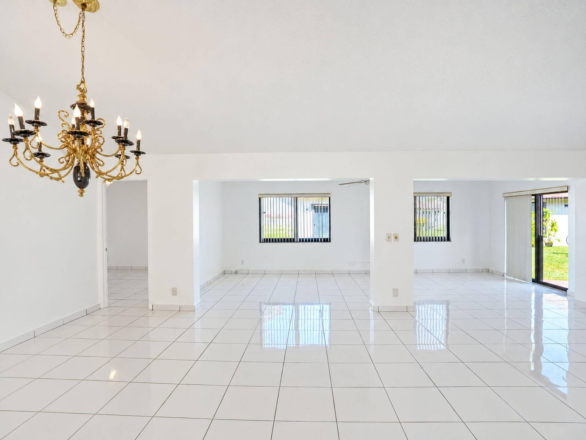 2079 SW 16TH Circle, Deerfield Beach, FL 33442 Open-concept interior featuring white tile flooring, gold-tone multi-arm chandelier, and sliding glass door