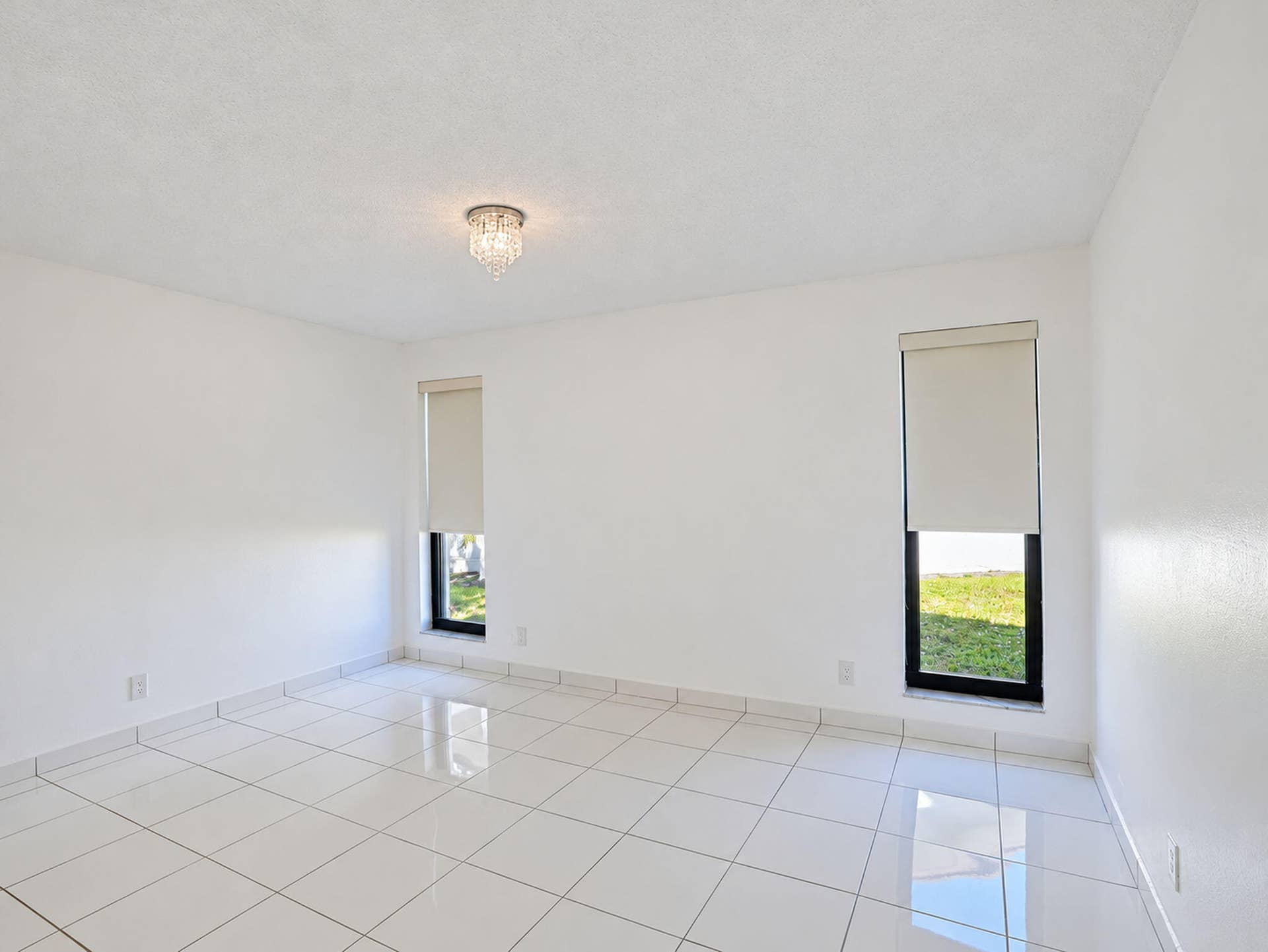 2079 SW 16TH Circle, Deerfield Beach, FL 33442 Neutral interior featuring large-format white tile flooring, dual floor-to-ceiling windows, roller shades, and a flush-mount crystal light fixture