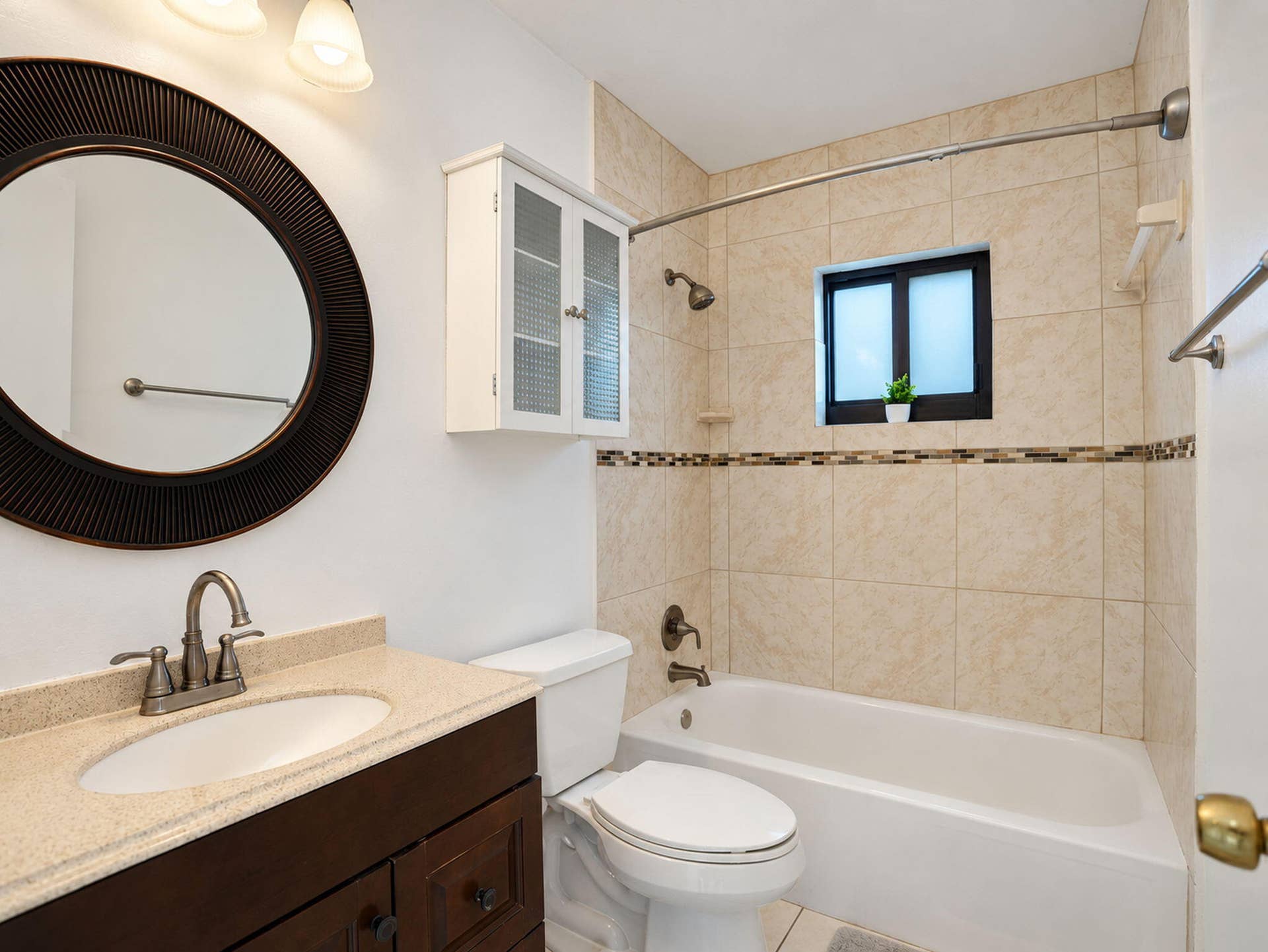 2079 SW 16TH Circle, Deerfield Beach, FL 33442 Bathroom featuring a dark wood vanity with a solid surface countertop, oval undermount sink, ceramic tile shower surround with decorative mosaic accent, and a white wall-mounted cabinet
