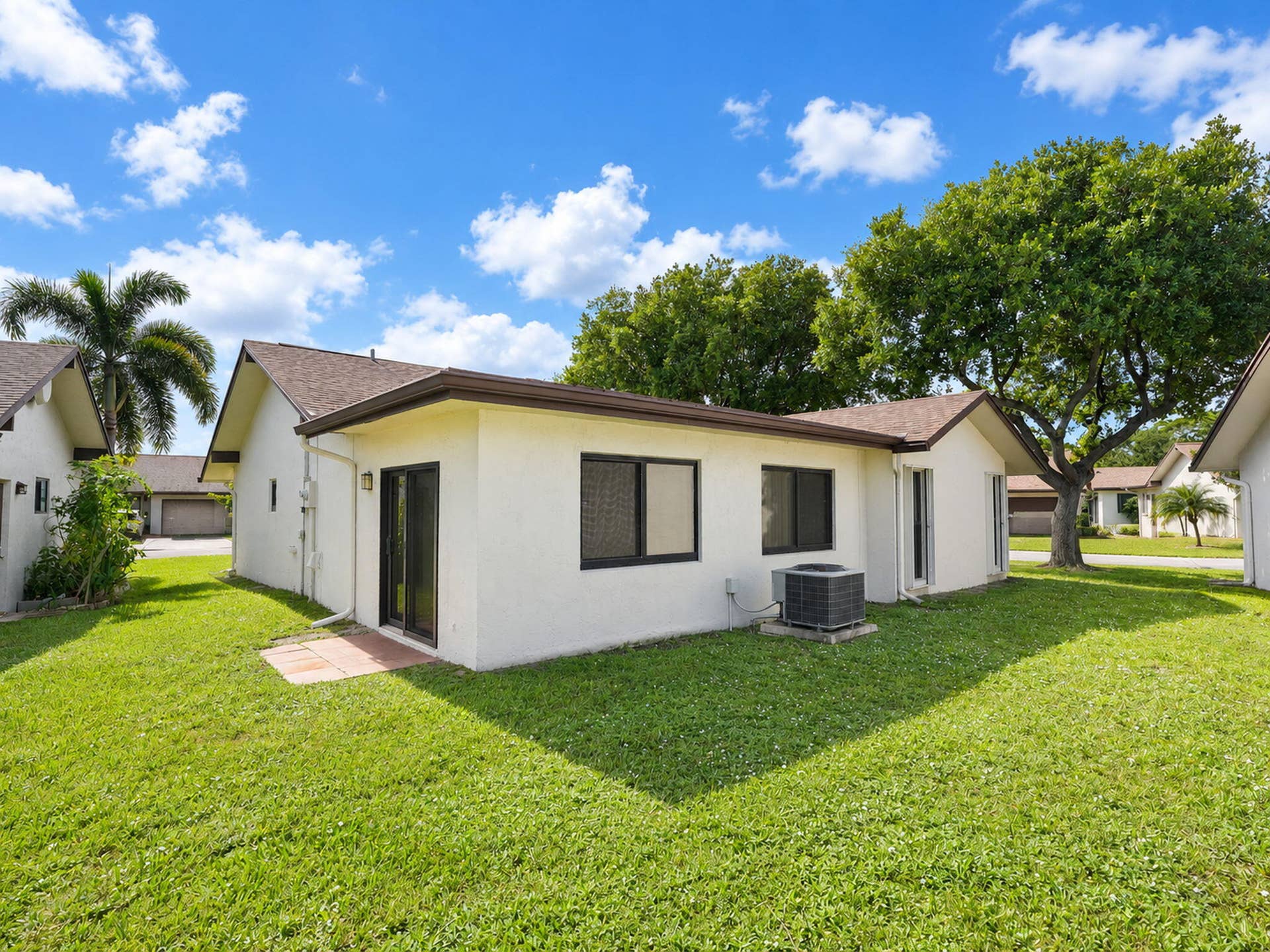 2079 SW 16TH Circle, Deerfield Beach, FL 33442 Stucco exterior featuring a gabled shingle roof, sliding glass doors, and expansive green space with mature trees