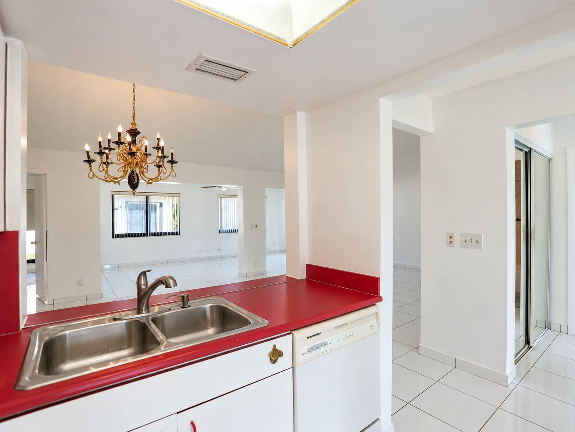 2079 SW 16TH Circle, Deerfield Beach, FL 33442 Kitchen featuring white cabinetry, solid-surface countertops, dual-basin stainless steel sink with high-arc faucet, integrated dishwasher, and overhead skylight
