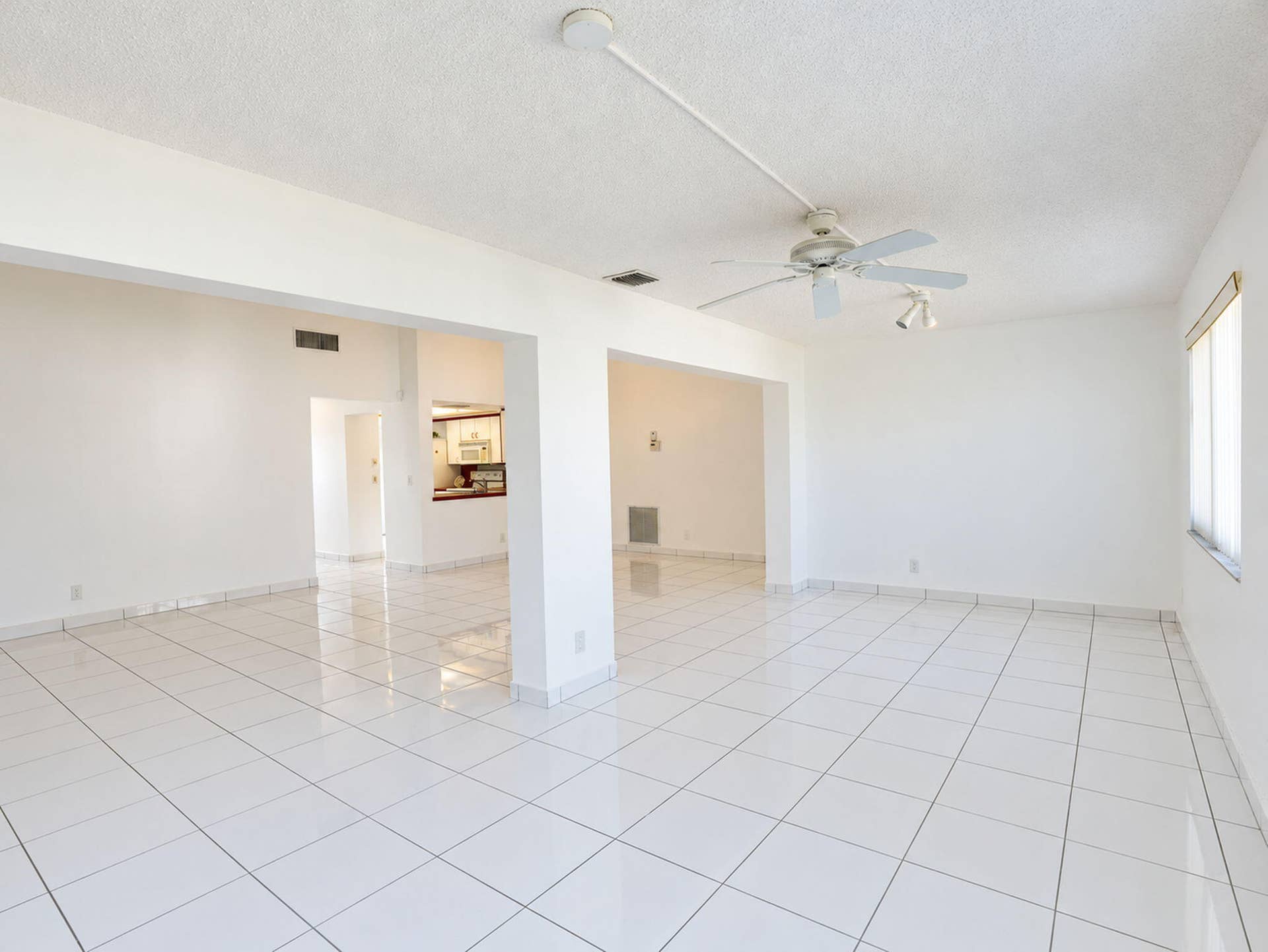 2079 SW 16TH Circle, Deerfield Beach, FL 33442 Open-concept interior featuring large-format white tile flooring, structural support pillars, a ceiling fan with integrated lighting, and horizontal window blinds