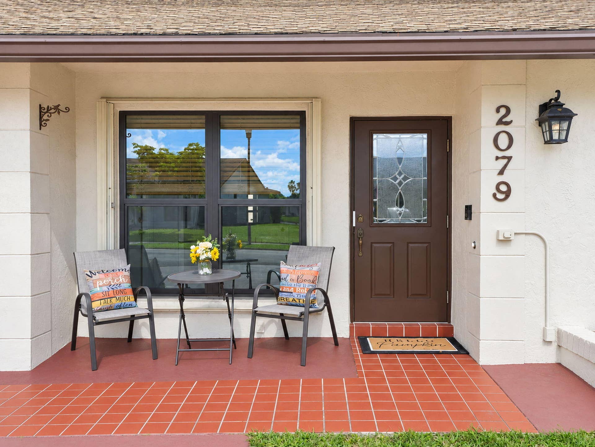 2079 SW 16TH Circle, Deerfield Beach, FL 33442 Stucco exterior entrance featuring a tile-paved porch, a solid door with an integrated glass inlay, and an attached traditional-style sconce