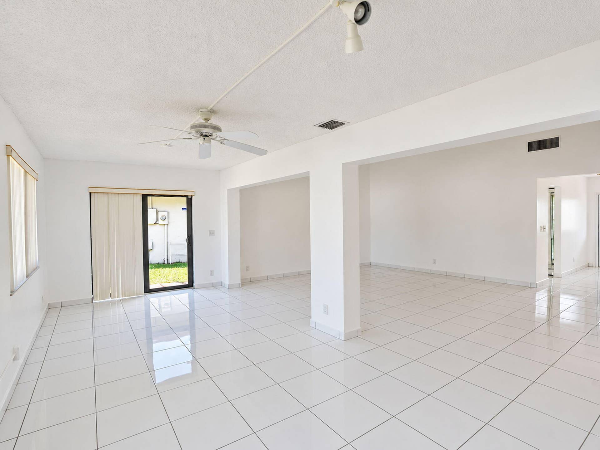 2079 SW 16TH Circle, Deerfield Beach, FL 33442 Open interior space featuring high-gloss ceramic tile flooring, a ceiling fan with integrated lighting, and glass sliding doors providing exterior access
