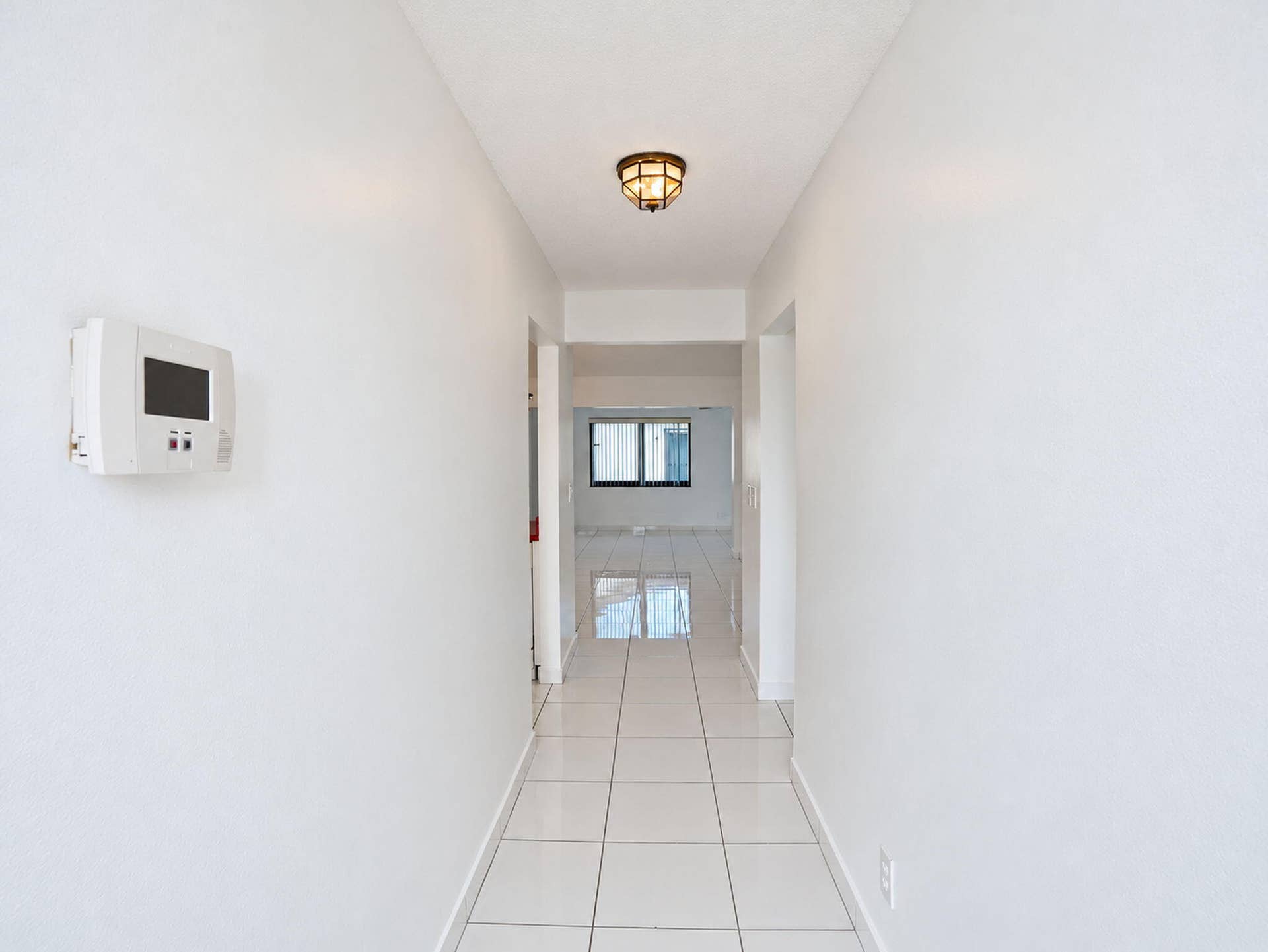 2079 SW 16TH Circle, Deerfield Beach, FL 33442 Hallway featuring neutral-toned tile flooring, flush-mount lighting, and a wall-mounted programmable thermostat