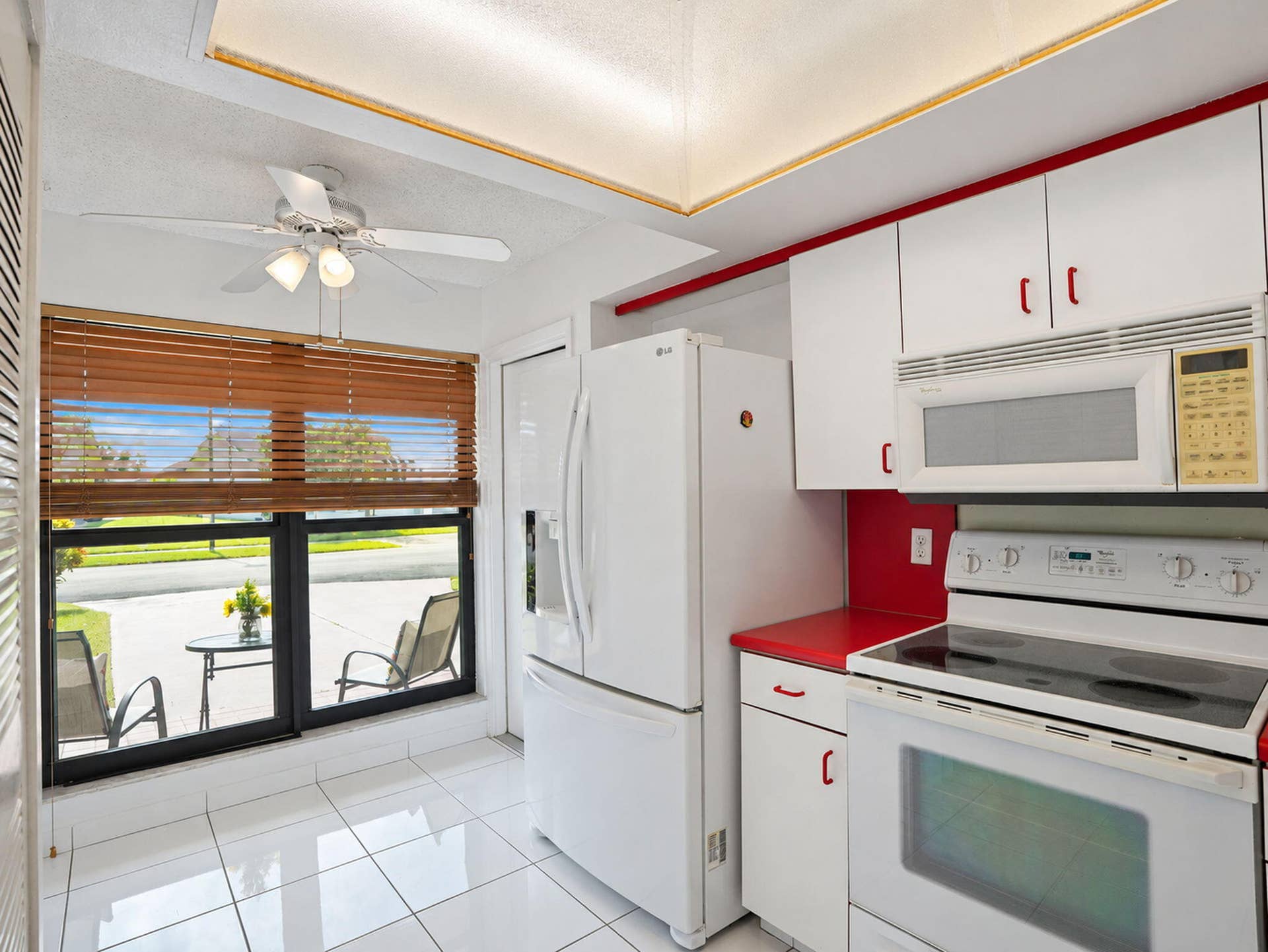 2079 SW 16TH Circle, Deerfield Beach, FL 33442 Kitchen featuring white cabinetry, contrasting red countertops, tiled flooring, a tray ceiling with integrated lighting, and a large window with wood-finish blinds
