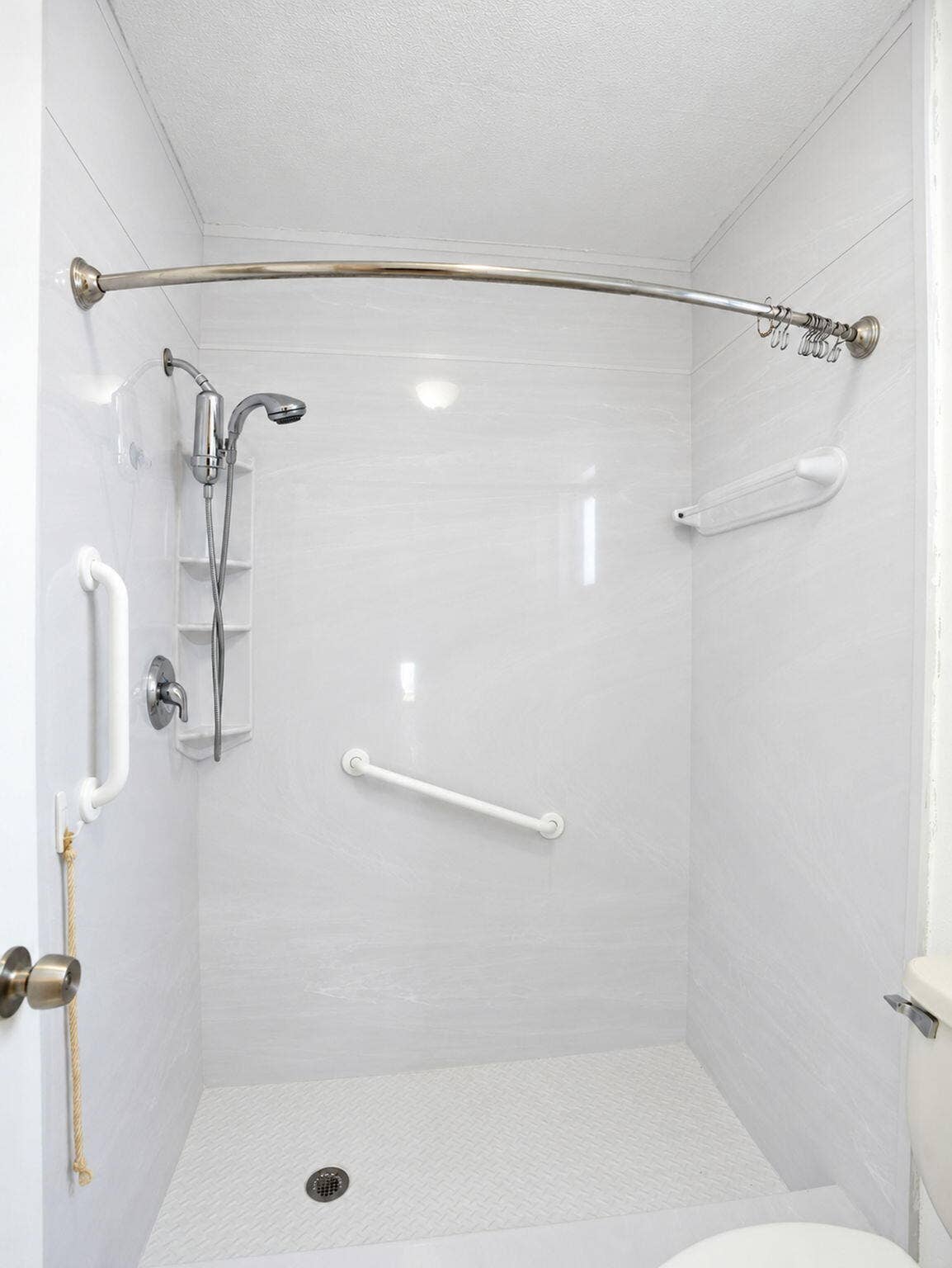 2079 SW 16TH Circle, Deerfield Beach, FL 33442 Walk-in shower enclosure featuring white wall panels, a handheld shower fixture, a curved shower rod, and integrated support bars
